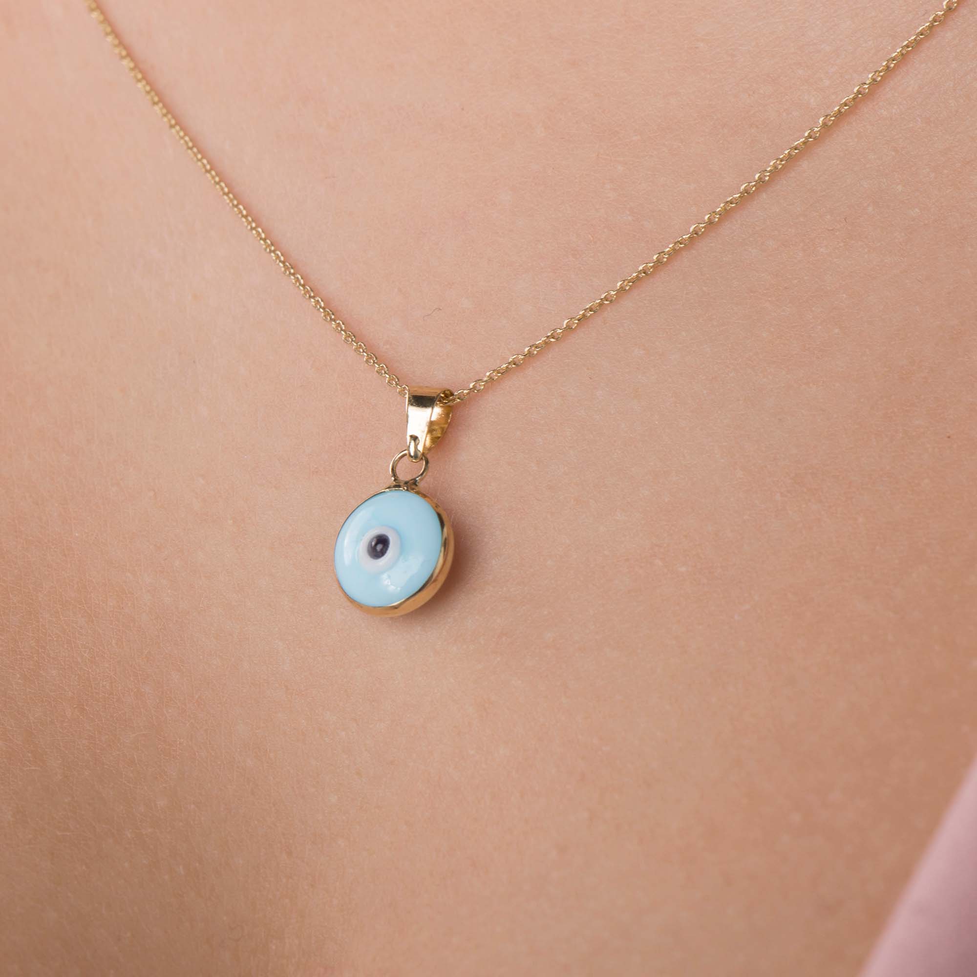 A model wearing a baby blue evil eye pendant on a chain shown up-close