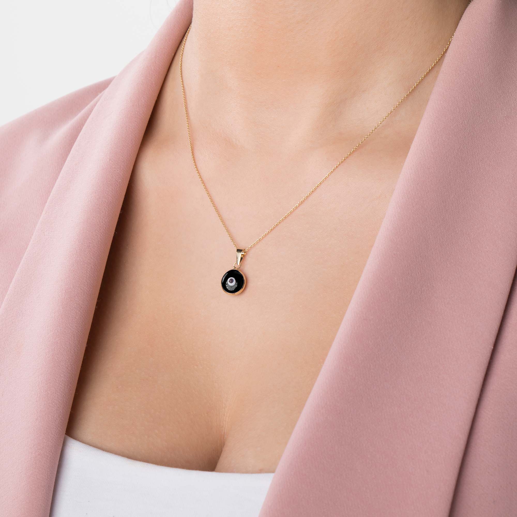 A model wearing a black evil eye pendant on a thin gold chain