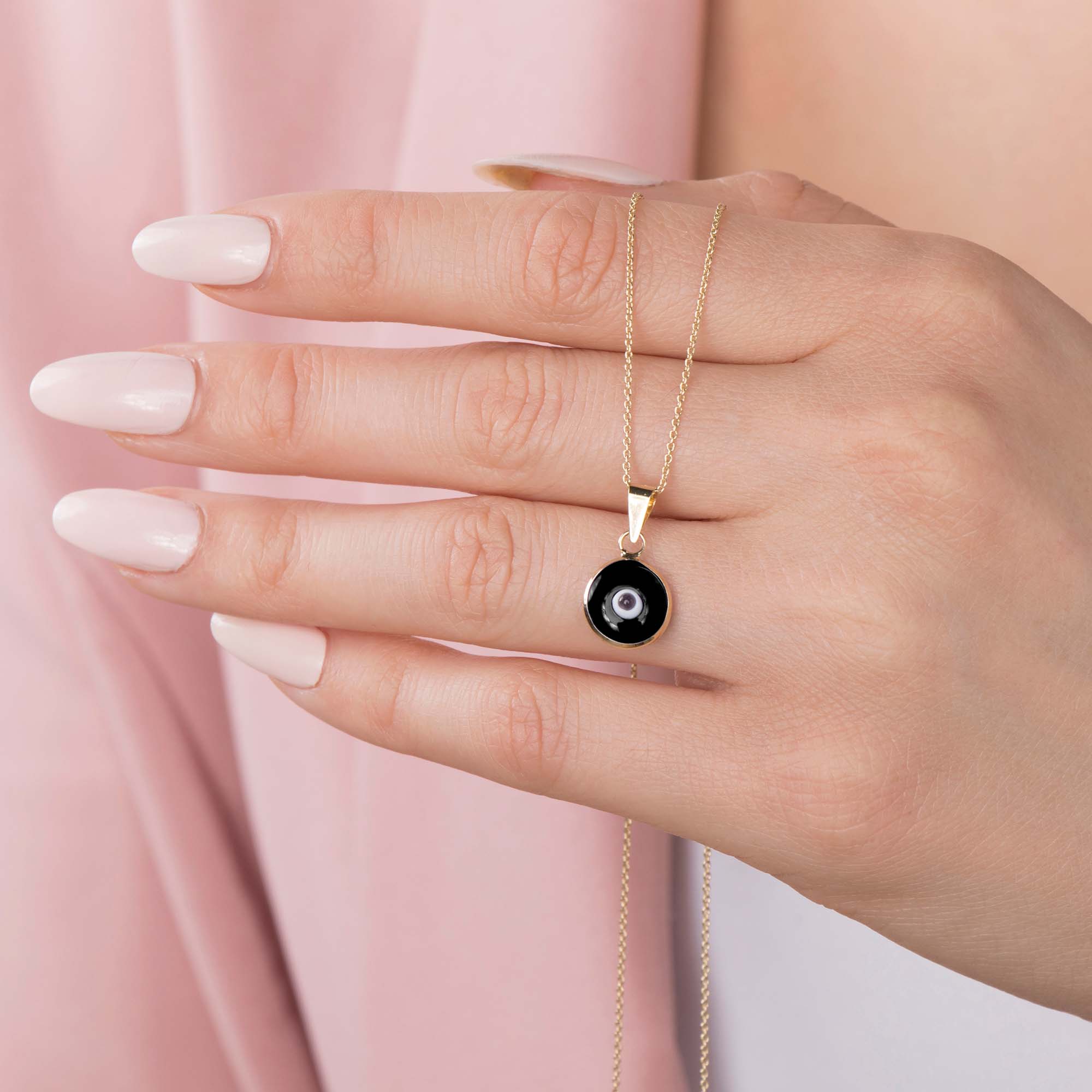 A hand holding a thin chain with a black evil eye pendant