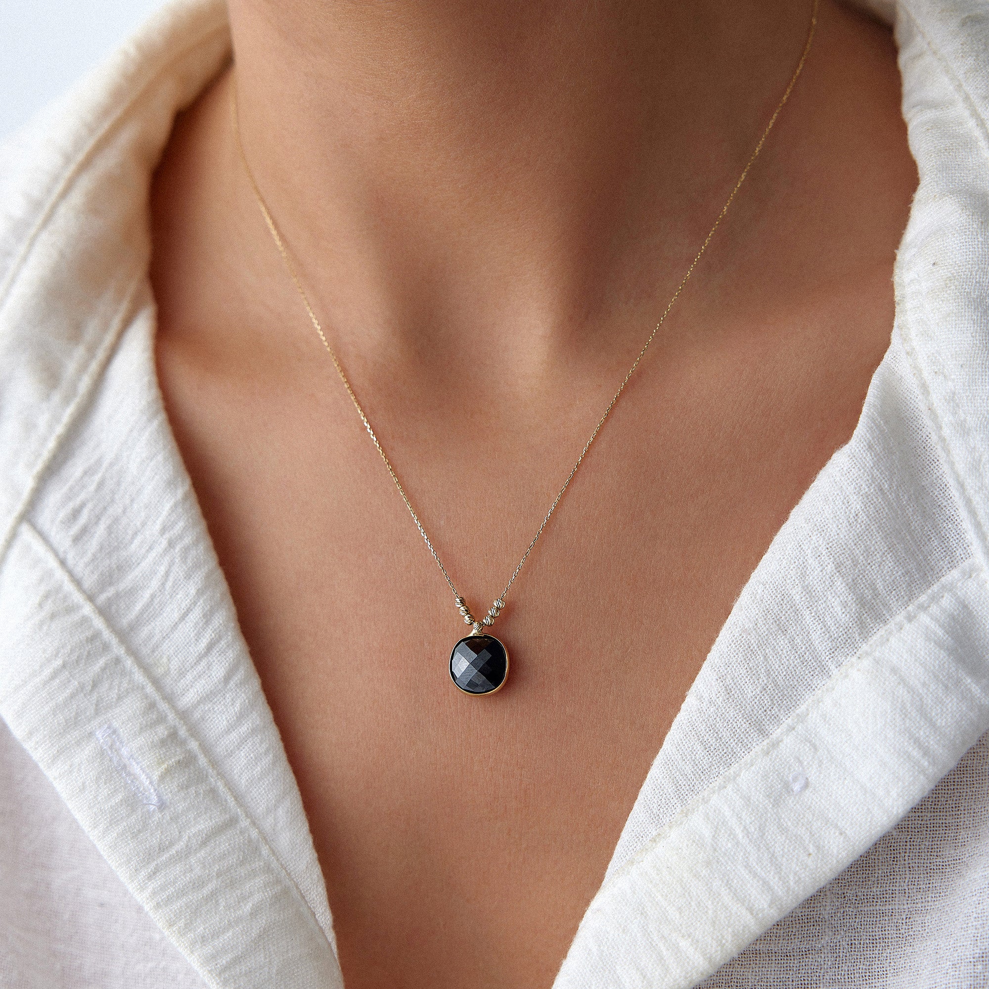 Necklace with a black crystal pendant worn by a person in a white outfit