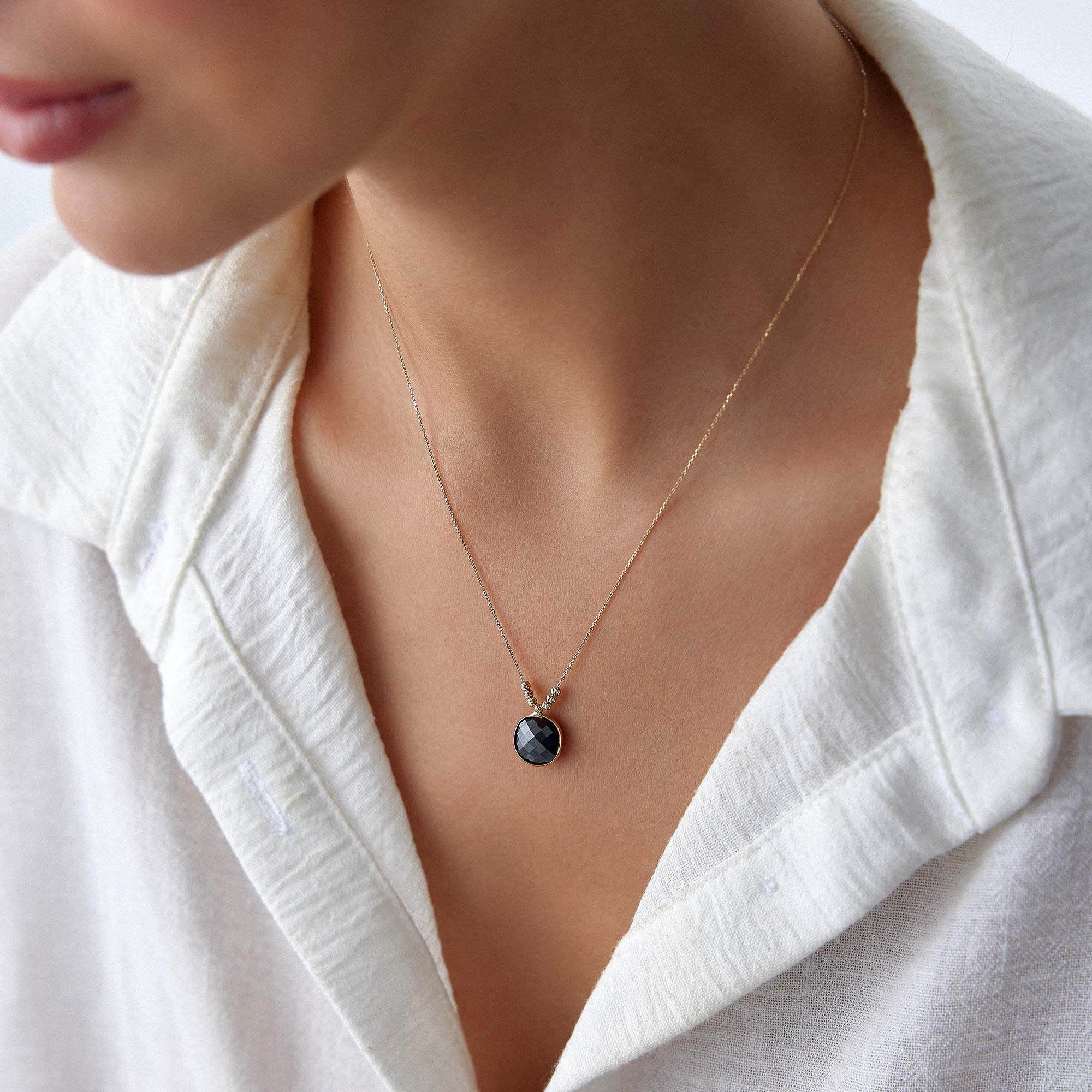 Necklace with a black crystal pendant worn by a person in a white outfit