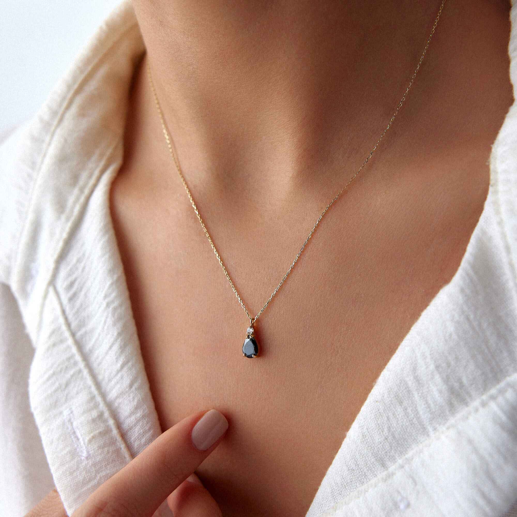 A close-up image of a model wearing a black drop necklace