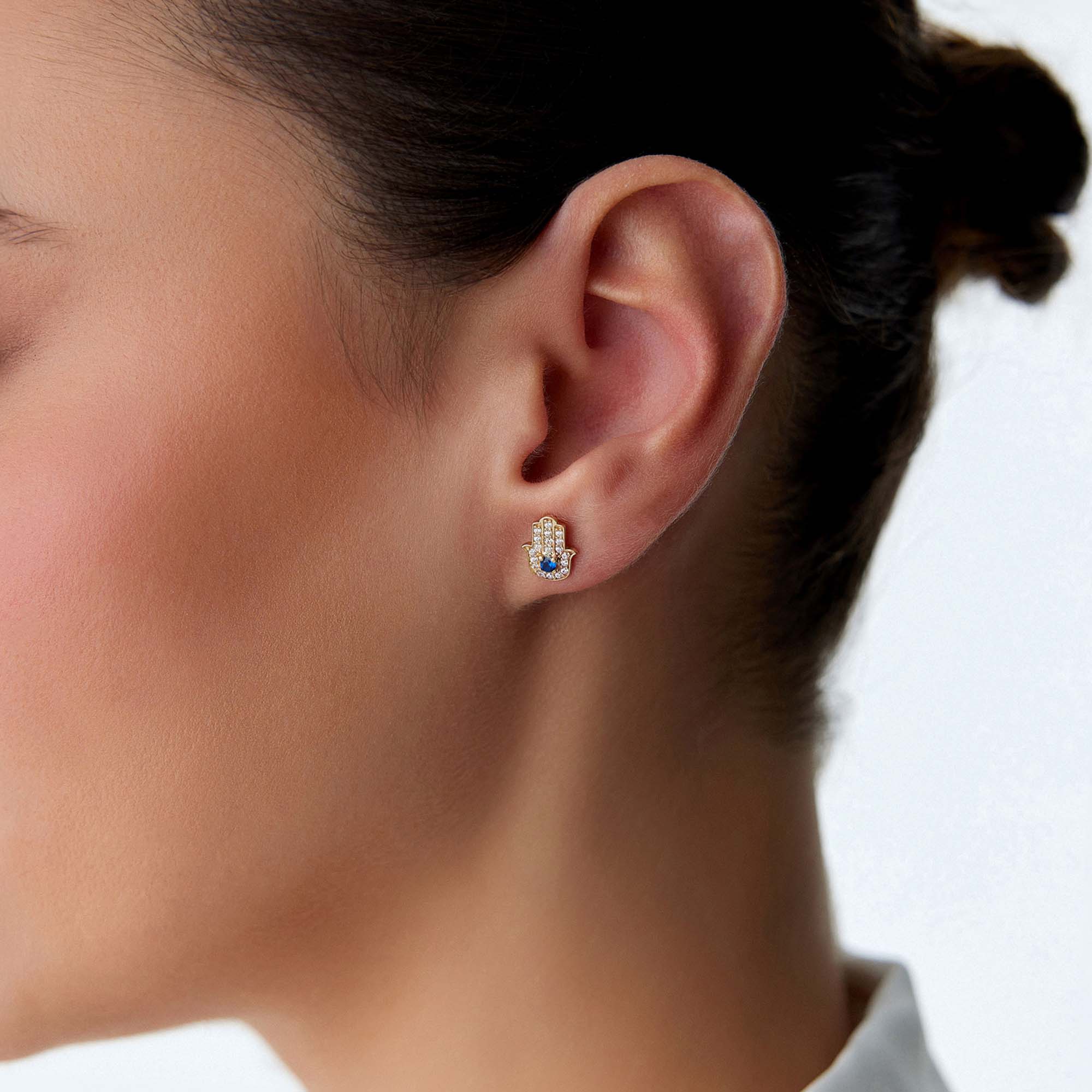 A model wearing a hamsa stud with a blue center