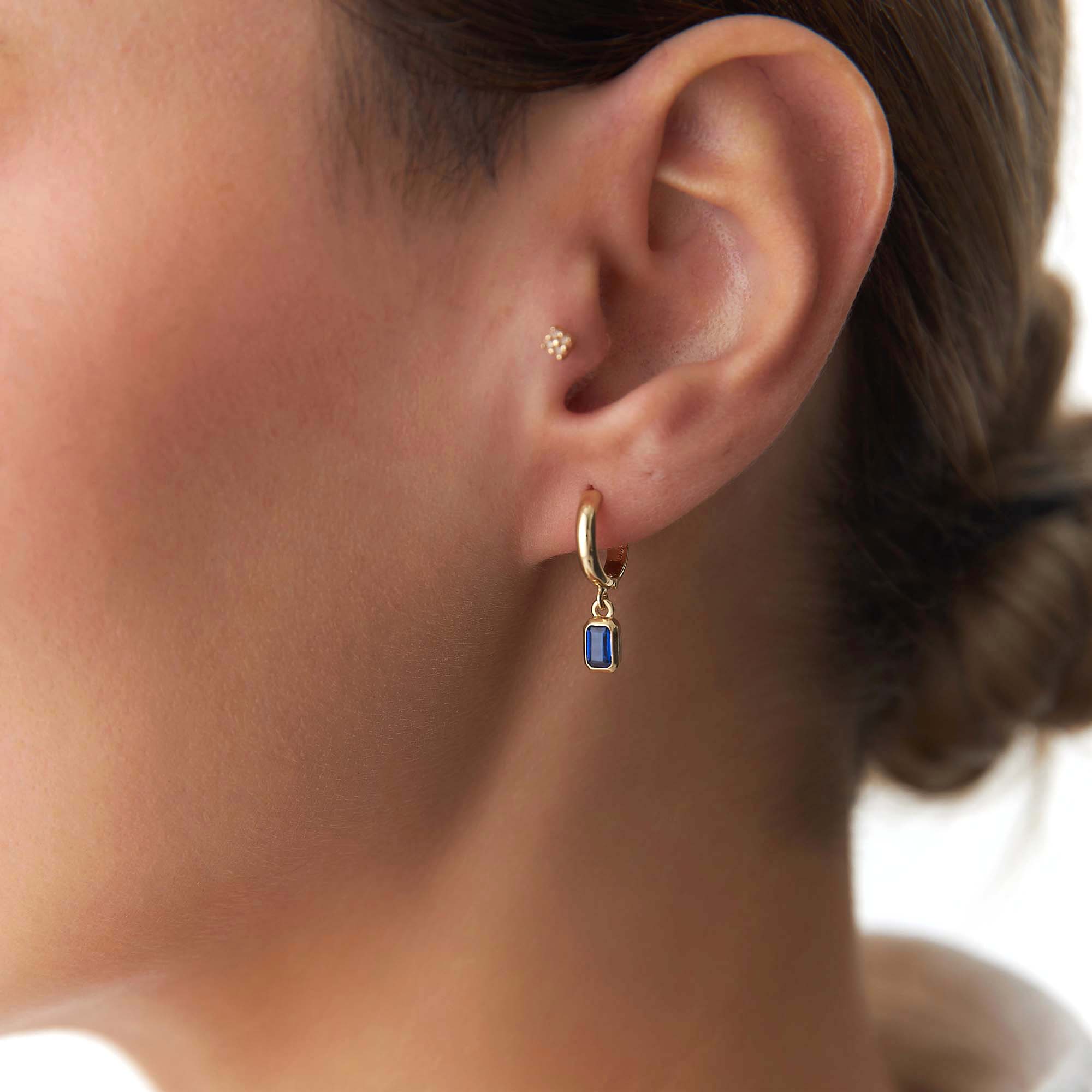Close-up of an ear wearing a gold hoop earring with a blue gemstone.