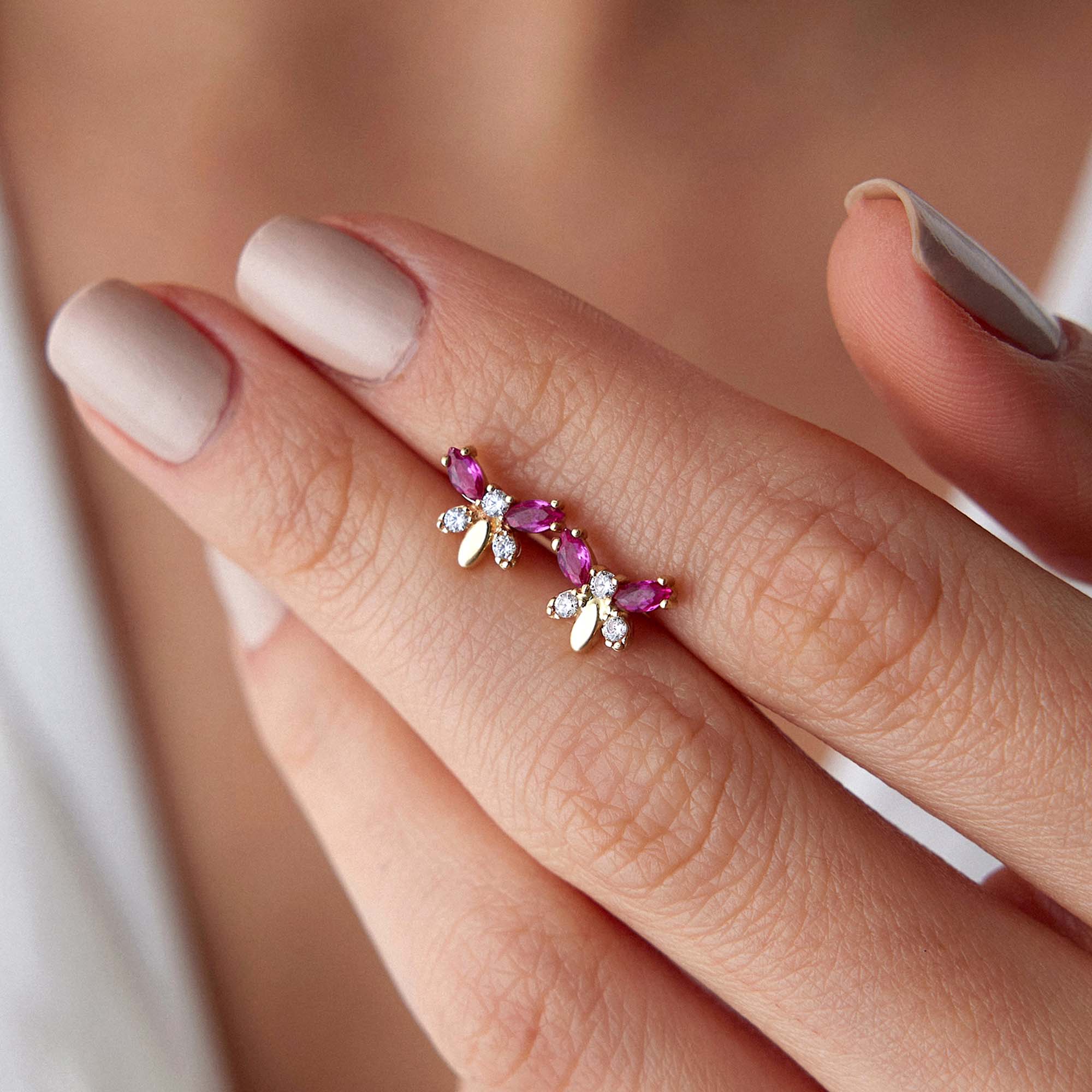 Close-up of a hand holding butterfly studs pink gemstones on a neutral background