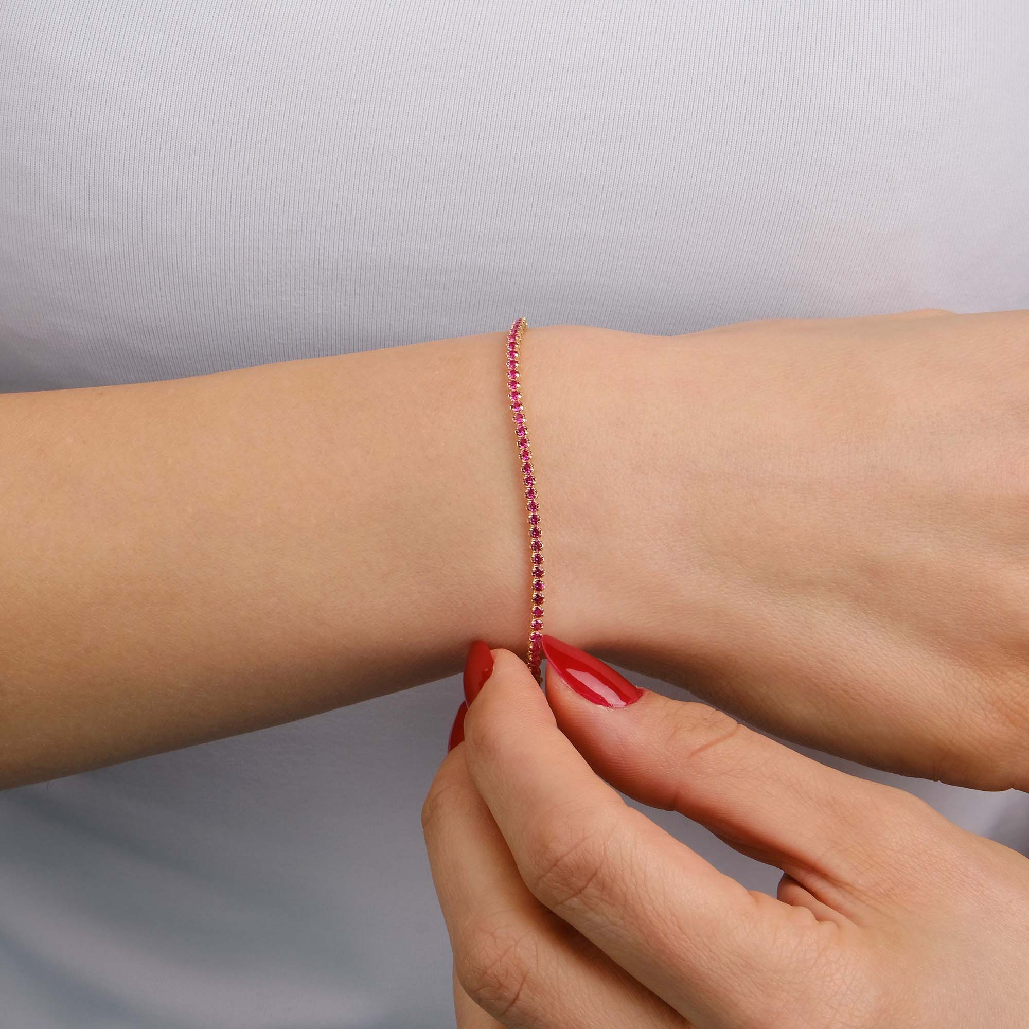 A created ruby tennis bracelet in 14K yellow gold with a width of 2.1 mm, featuring a series of red gemstones.