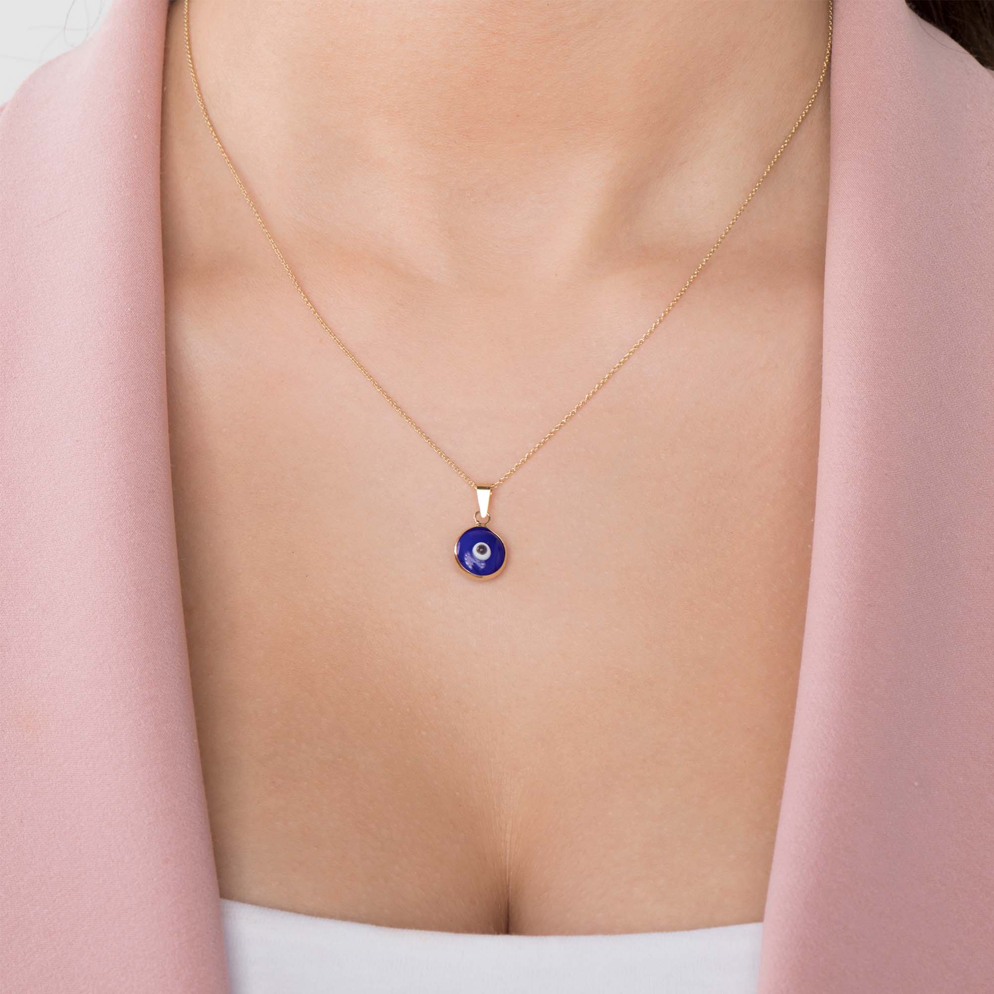 A model wearing a navy blue evil eye pendant on a thin gold chain