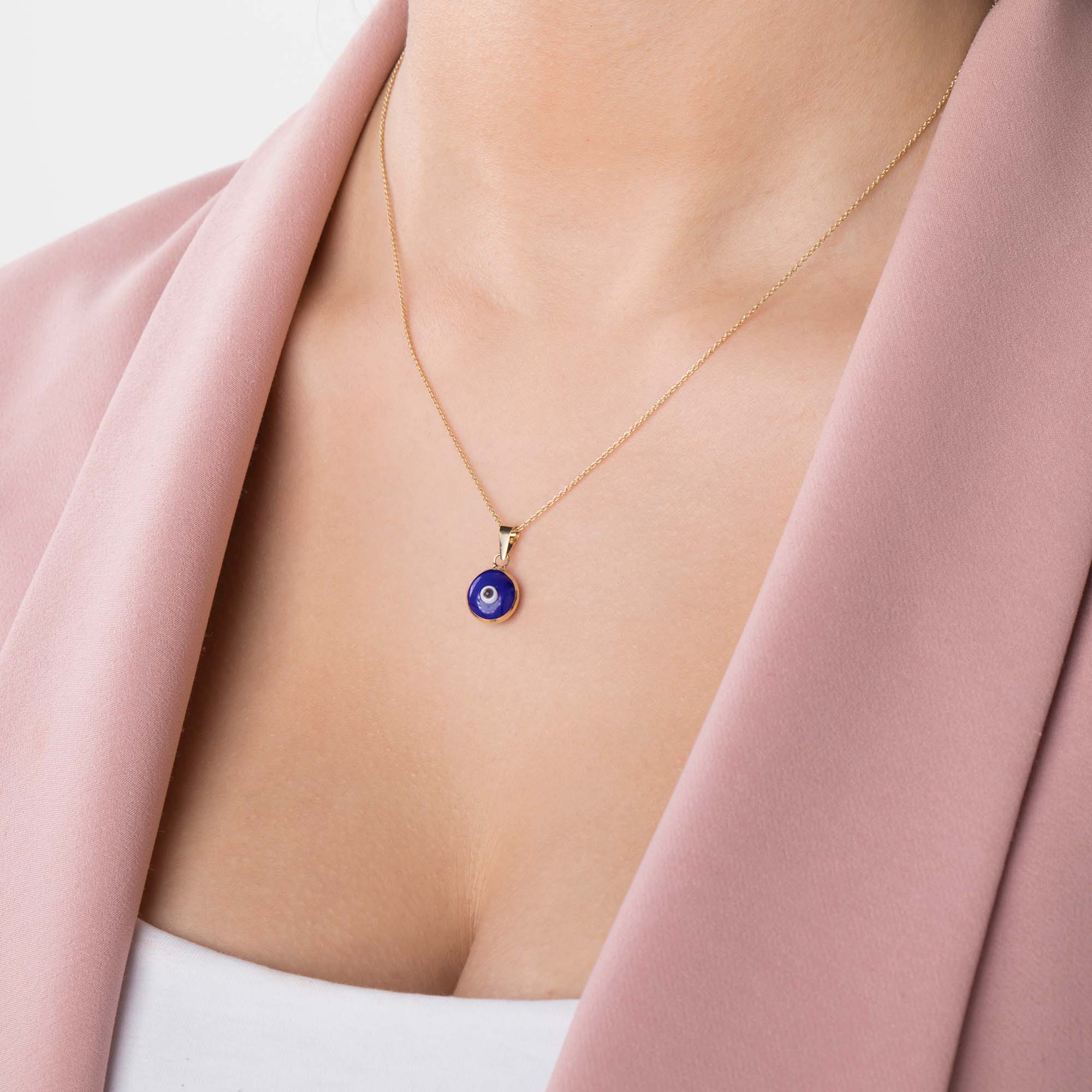 A model wearing a navy blue evil eye pendant on a thin gold chain