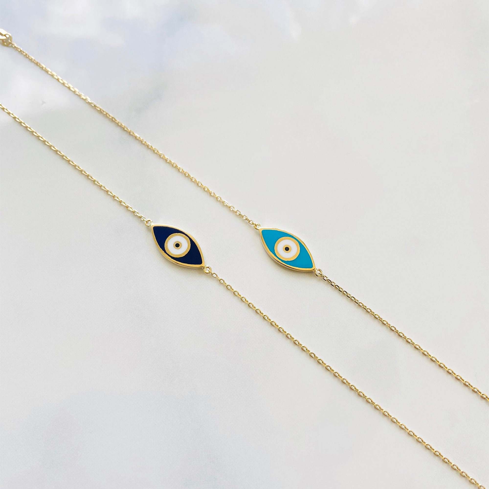 A double-sided evil eye bracelet with one side navy blue and the other turquoise, set against a yellow gold chain on a white background.