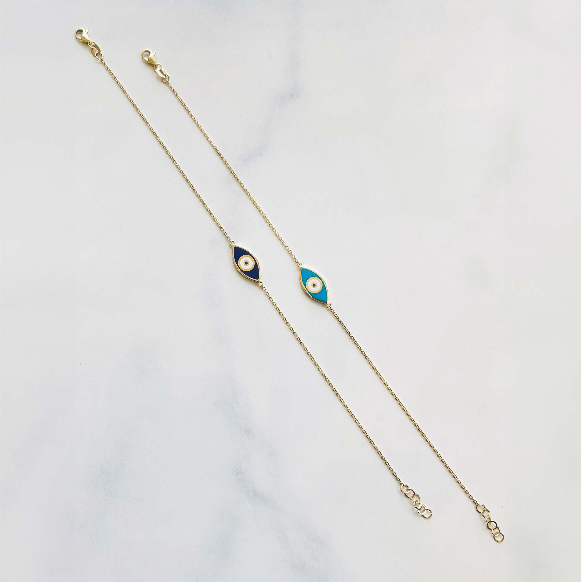 A double-sided evil eye bracelet with one side navy blue and the other turquoise, set against a yellow gold chain on a white background.