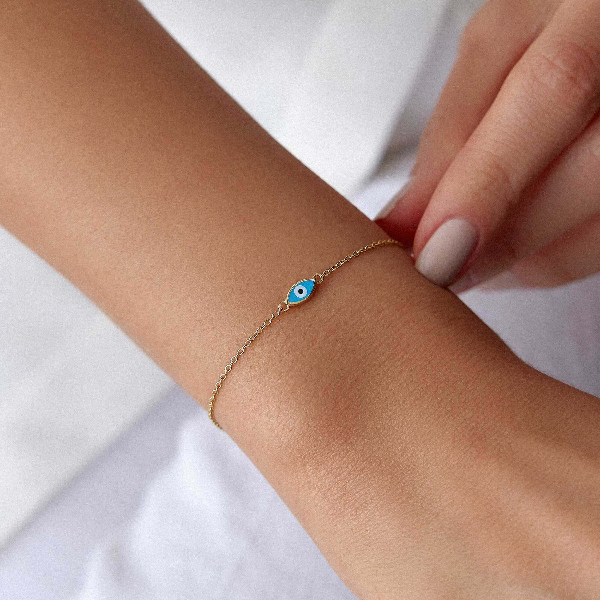 Gold bracelet with a blue eye charm on a wrist against a white background