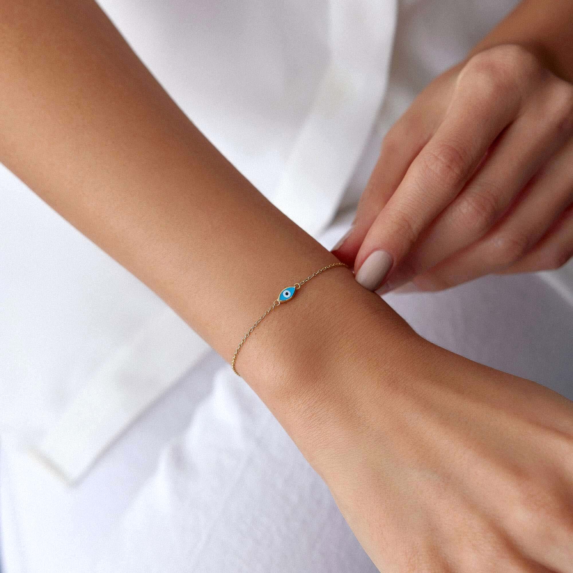 Gold bracelet with a blue evil eye on a person's wrist against a white background