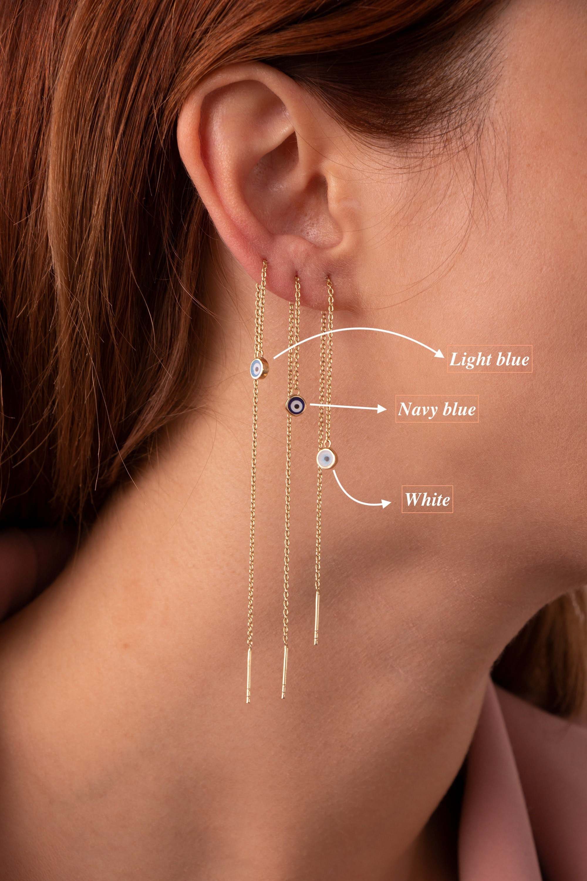 A pair of evil eye threader earrings in 14K gold, featuring a dainty and minimal design, displayed on a person's ear.