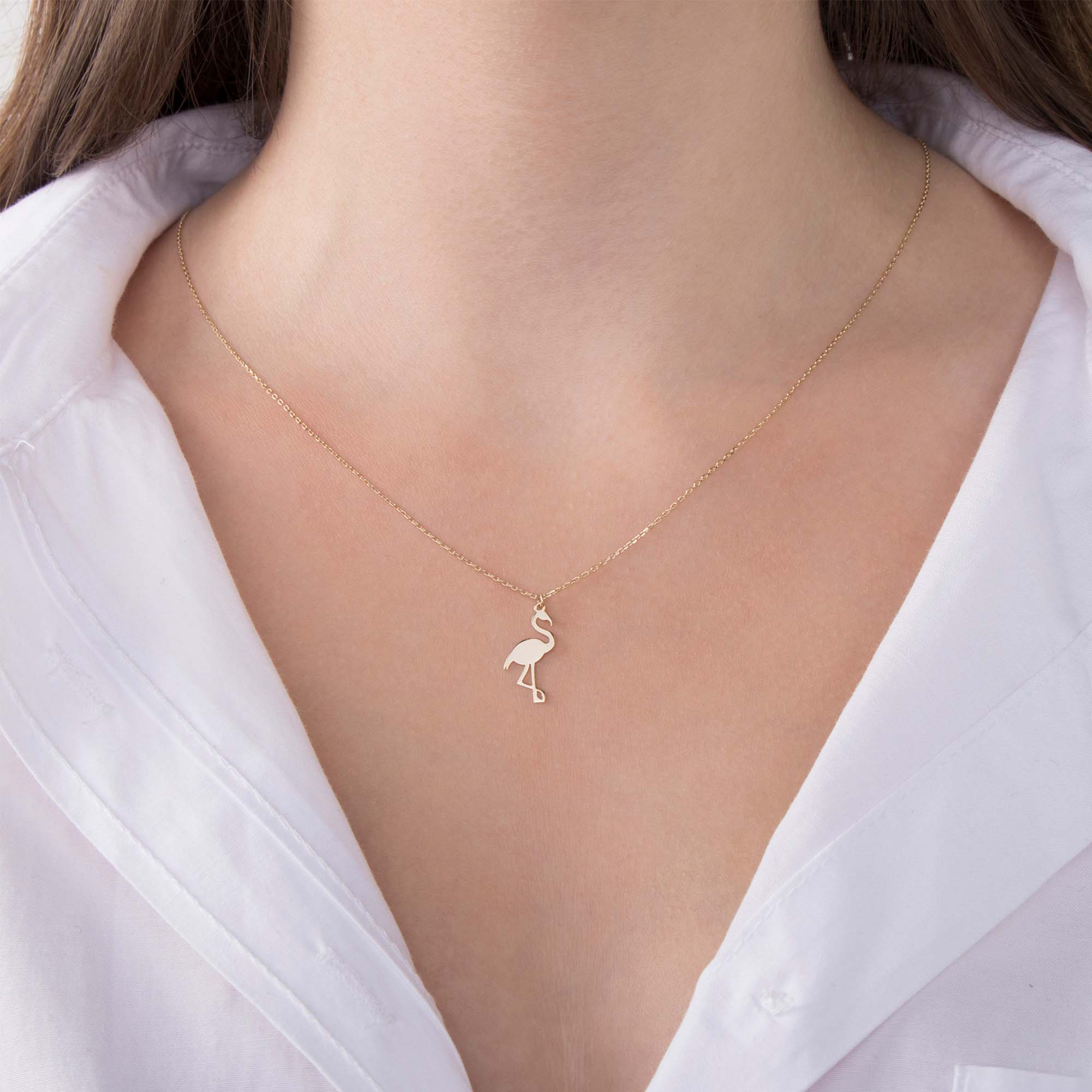 Gold flamingo pendant necklace on a person wearing a white shirt
