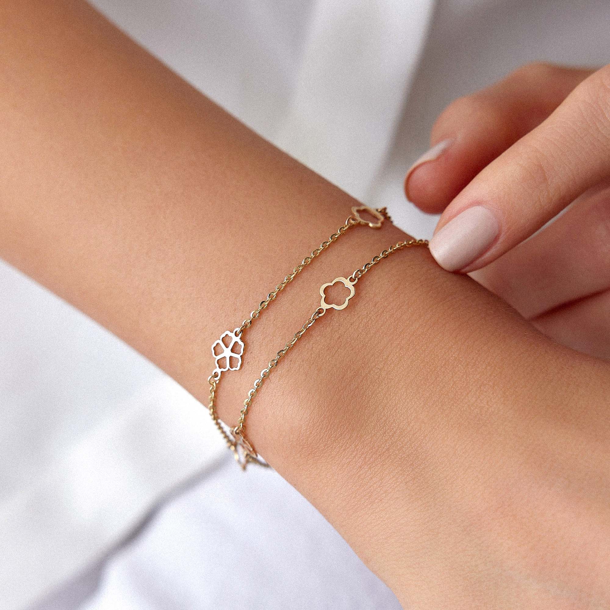 14K gold bracelet with flower-shaped charms on a wrist against a white background