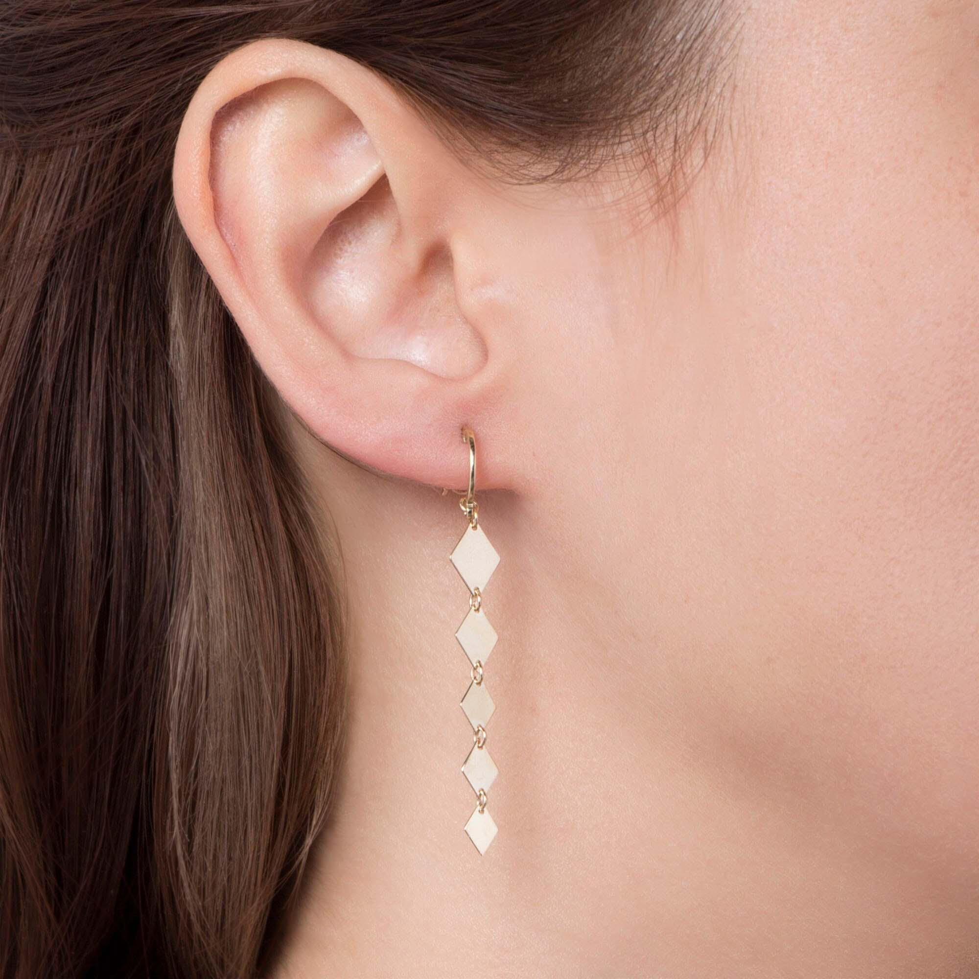 Close-up of an ear wearing a gold earring with diamond-shaped beads.