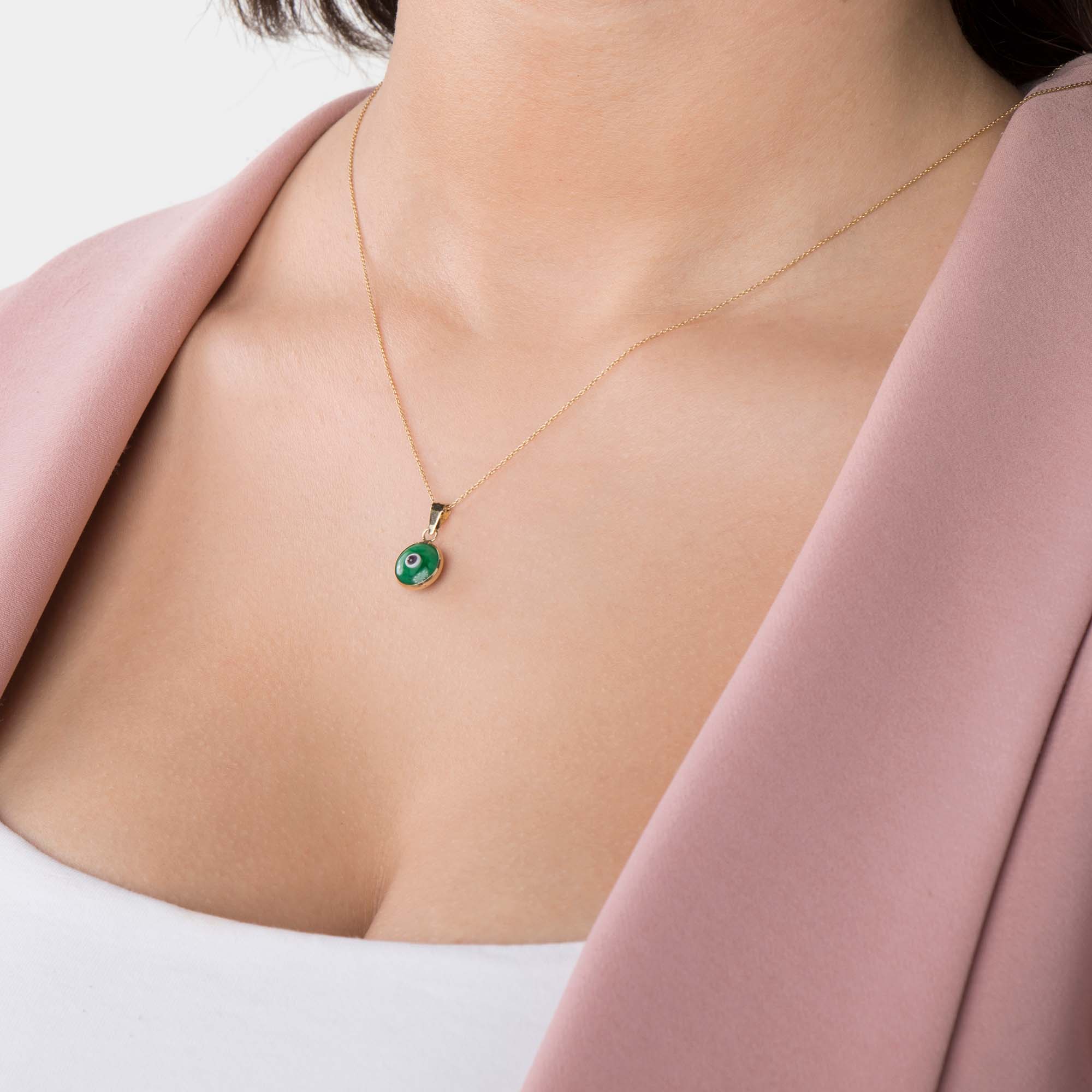 Necklace with a green evil eye pendant worn by a person against a neutral background