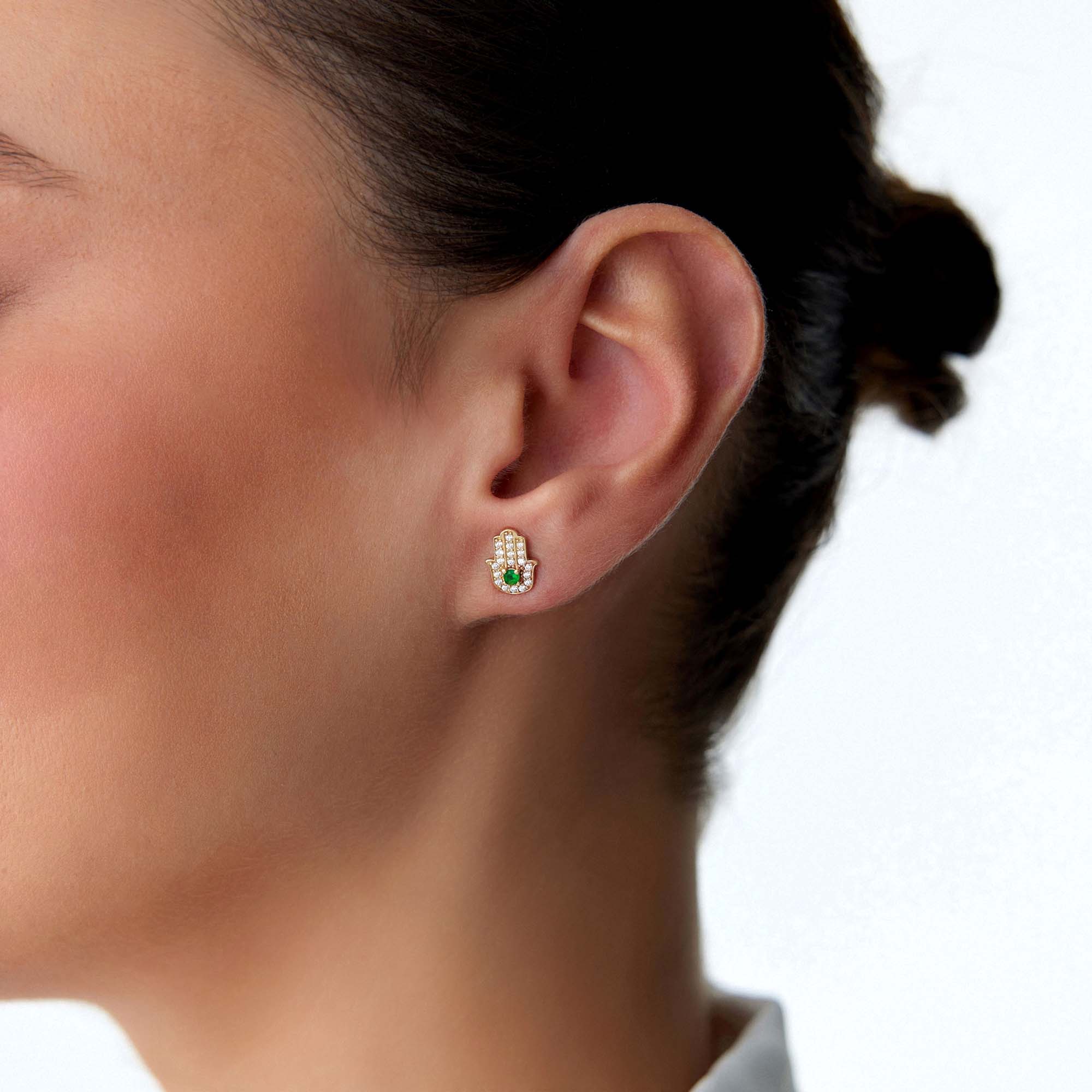 Close-up of an ear wearing a green hamsa stud with a blurred background