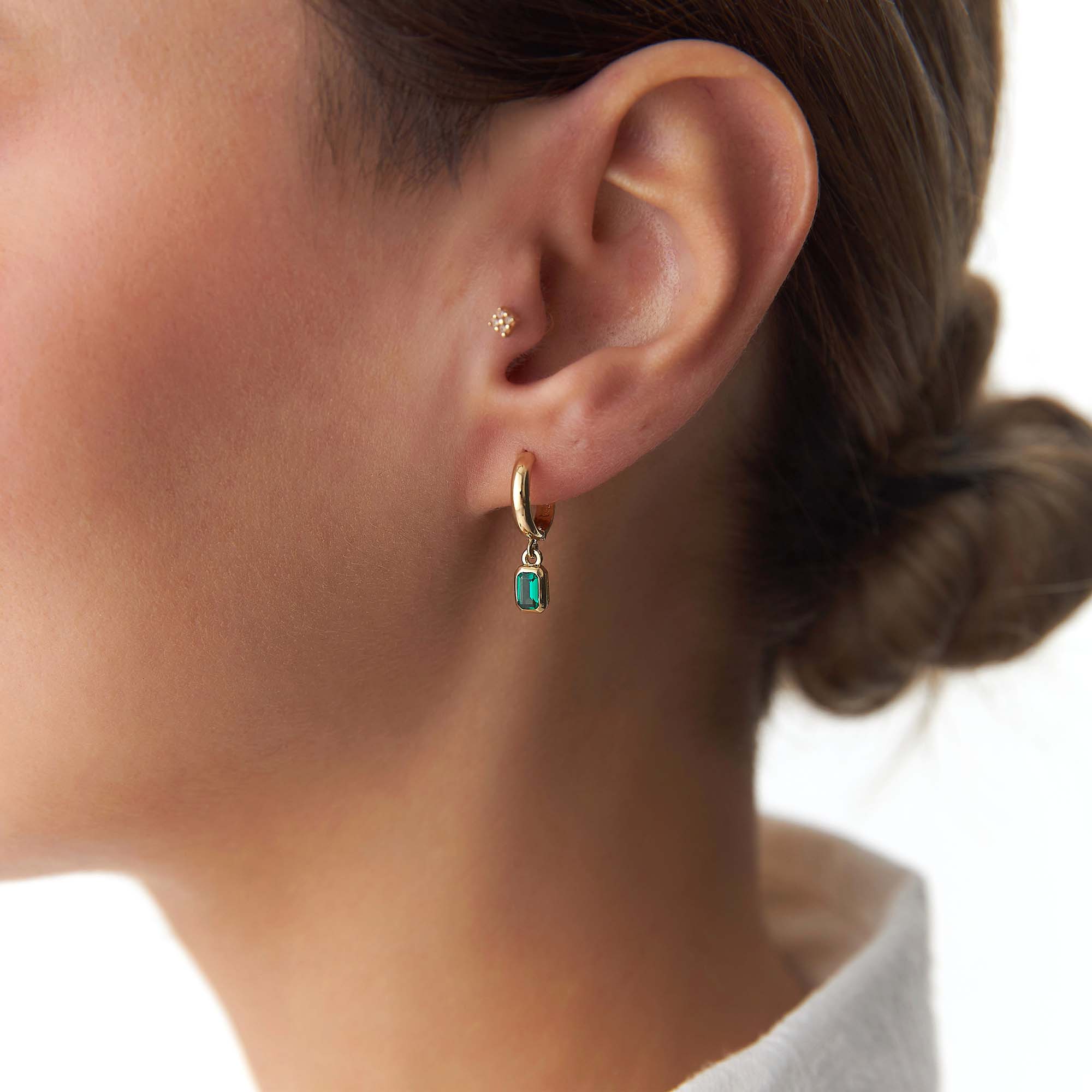 Close-up of an ear wearing a gold earring with a green gemstone on a blurred background