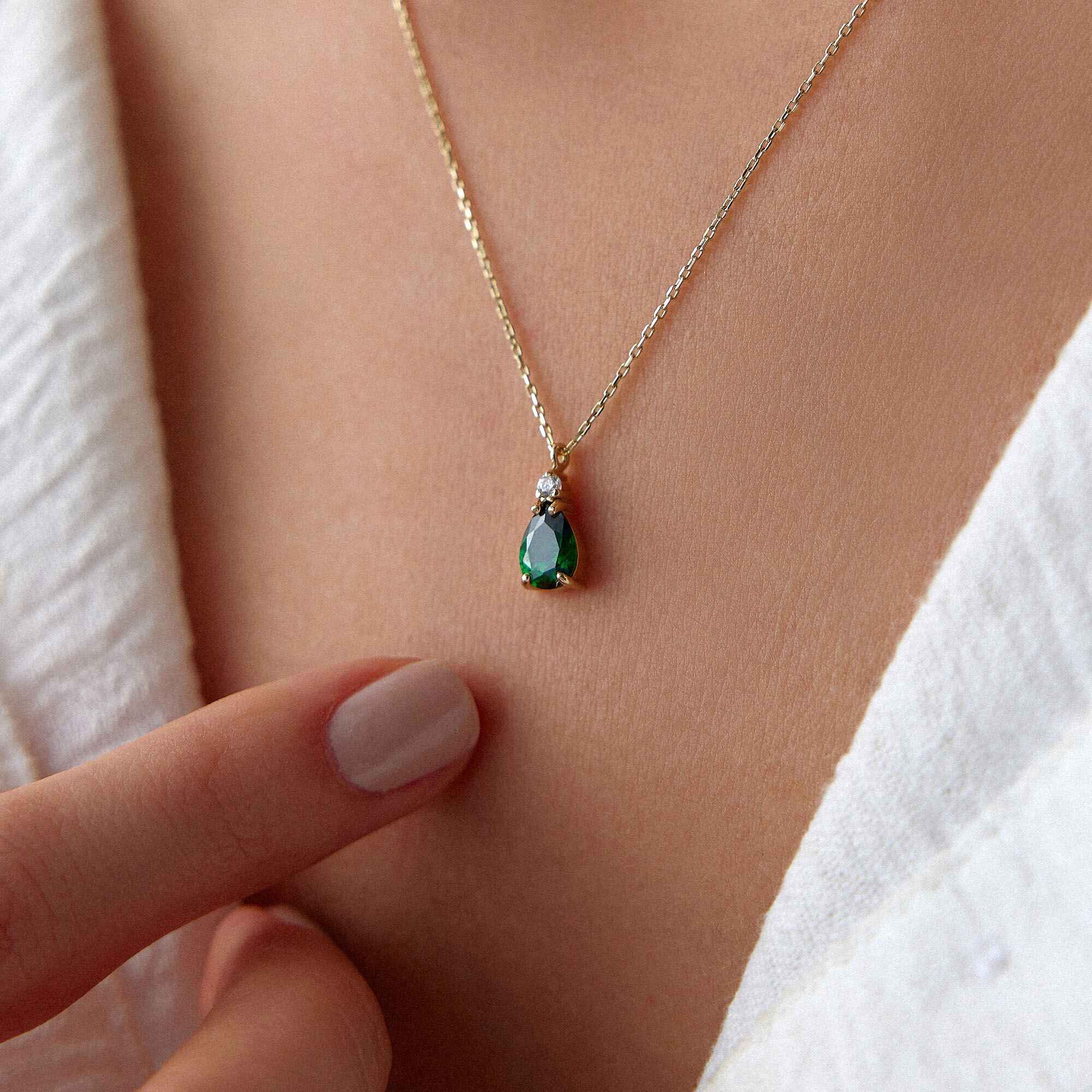 A close-up image of a model wearing a green drop necklace