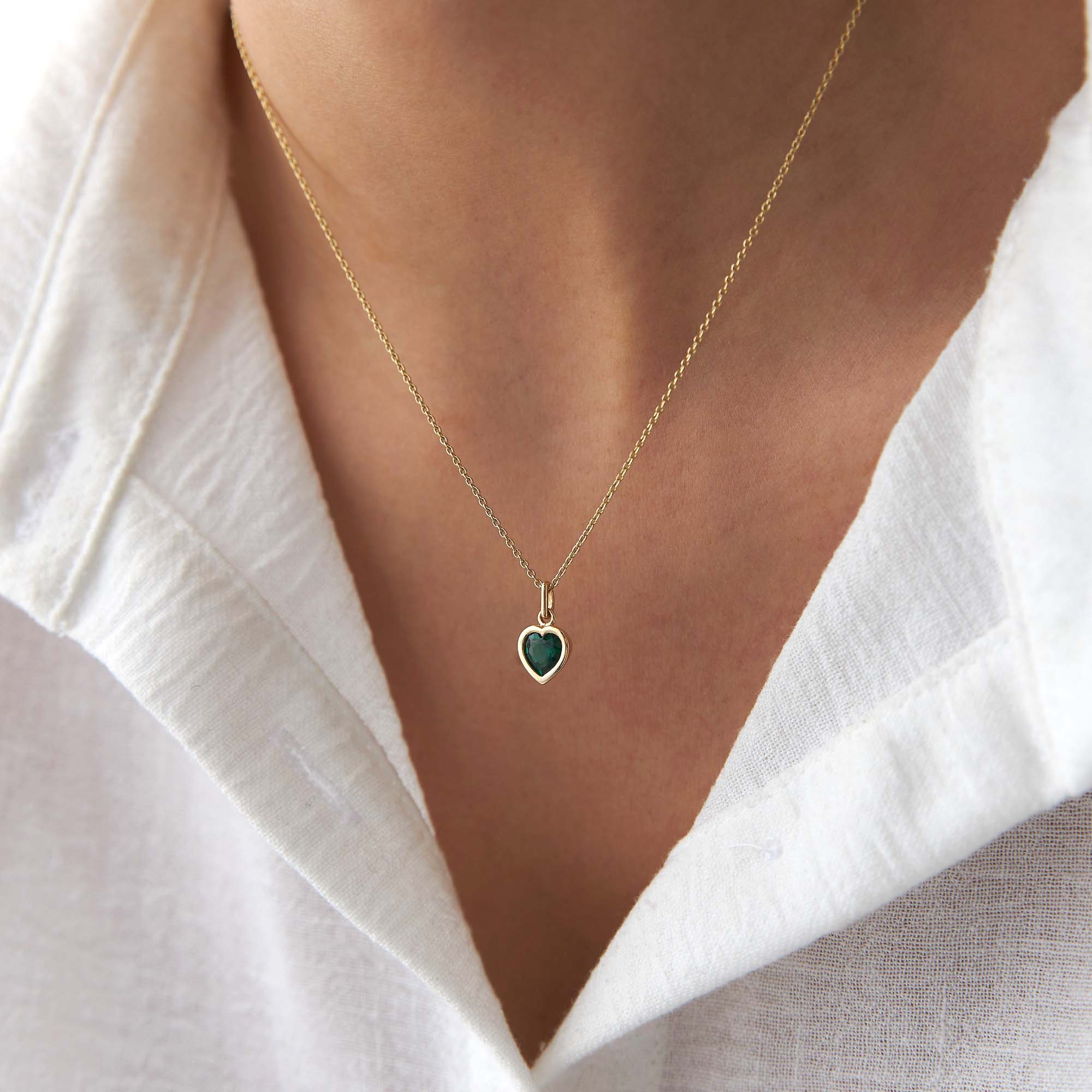 Gold necklace with a heart-shaped green pendant worn by a person in a white shirt.