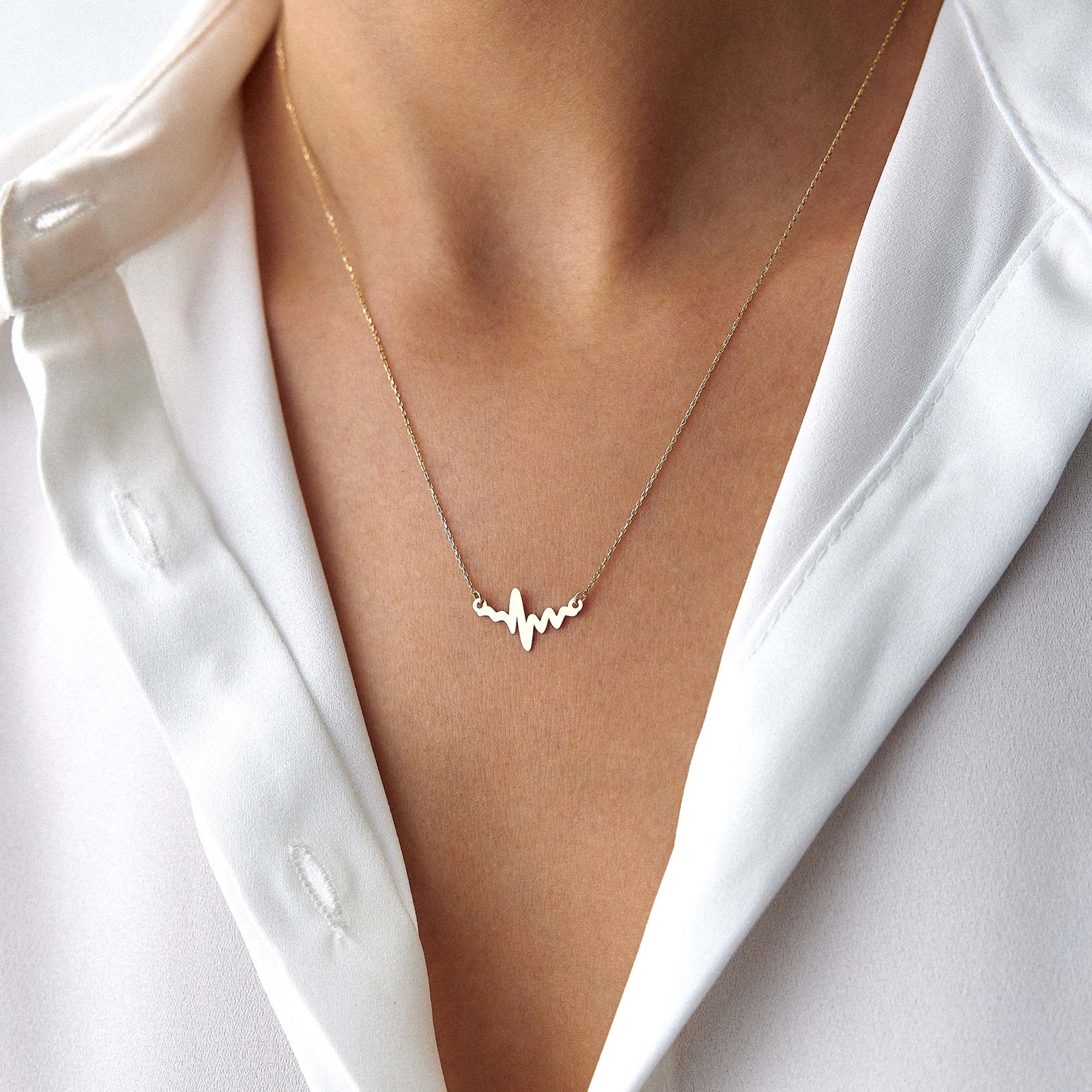 An upclose image of a model wearing a golden heartbeat necklace.