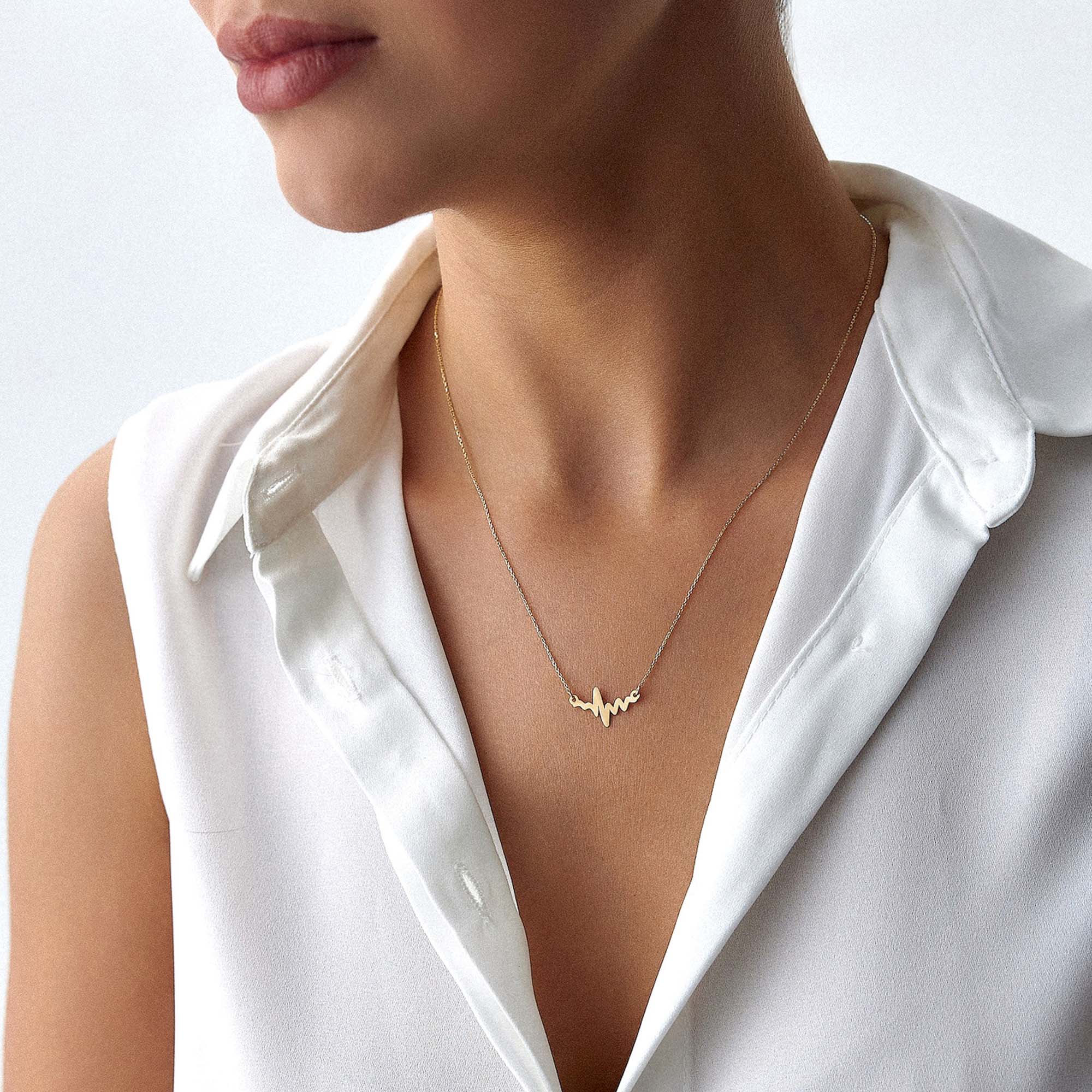 An image of a model wearing a golden heartbeat necklace.