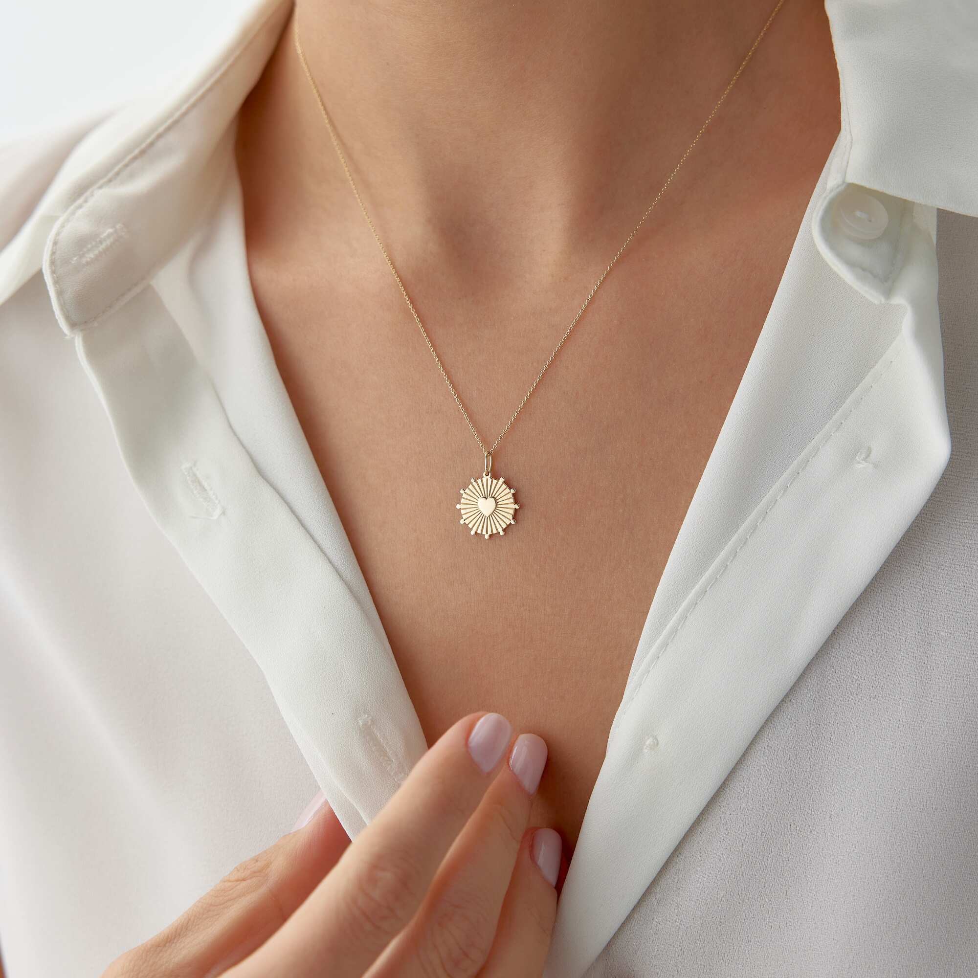 A model wearing a 14k yellow gold heartburst coin pendant on a thin gold chain.