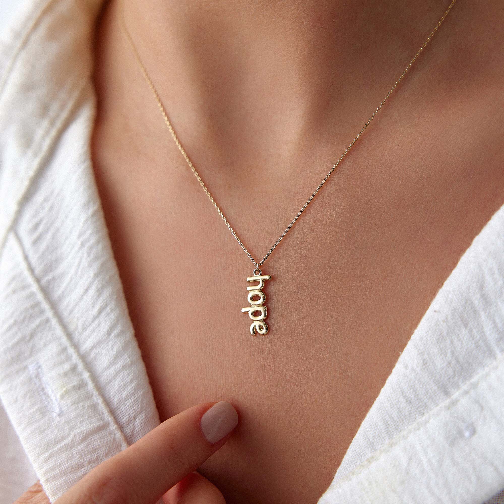 Gold 'hope' necklace on a person wearing a white shirt.