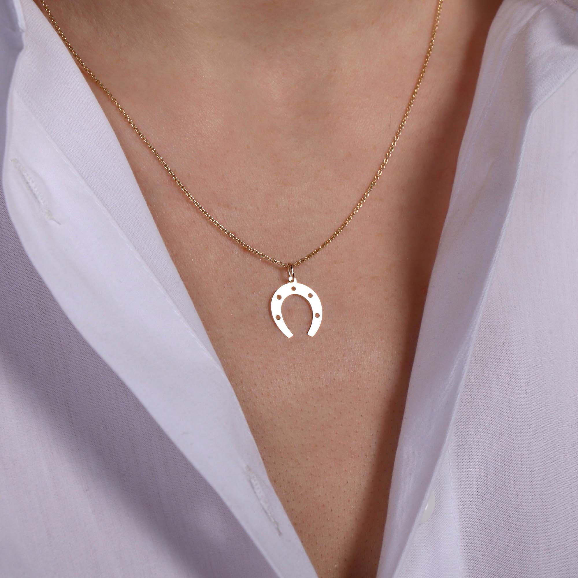 Gold necklace with a horseshoe pendant worn by a person in a white shirt.