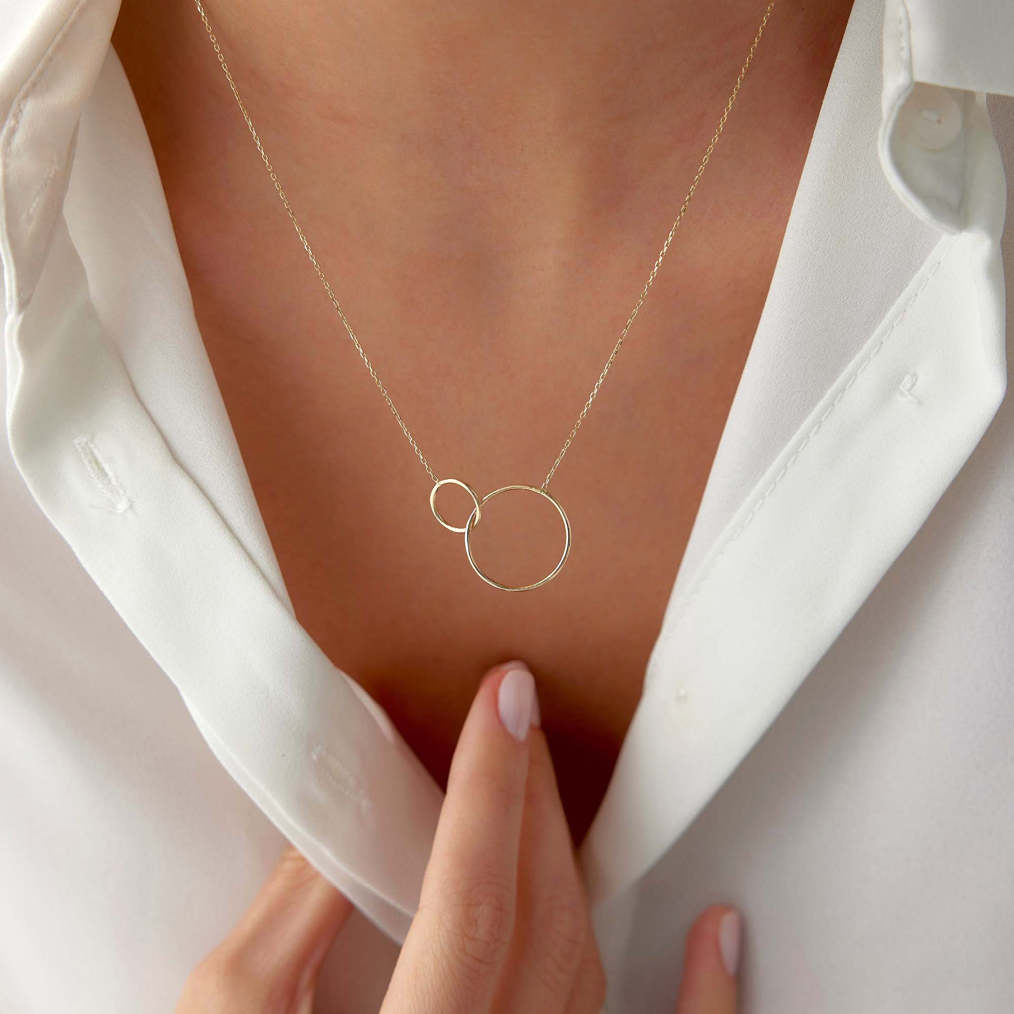 Gold necklace with interlocking rings worn by a person in a white shirt.