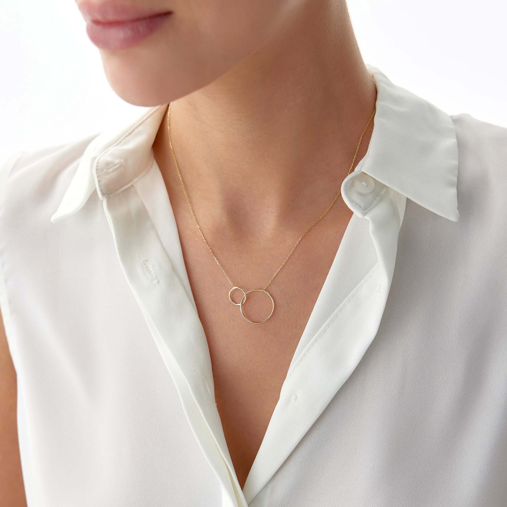 Gold necklace with interlocking rings worn by a person in a white shirt on a white background