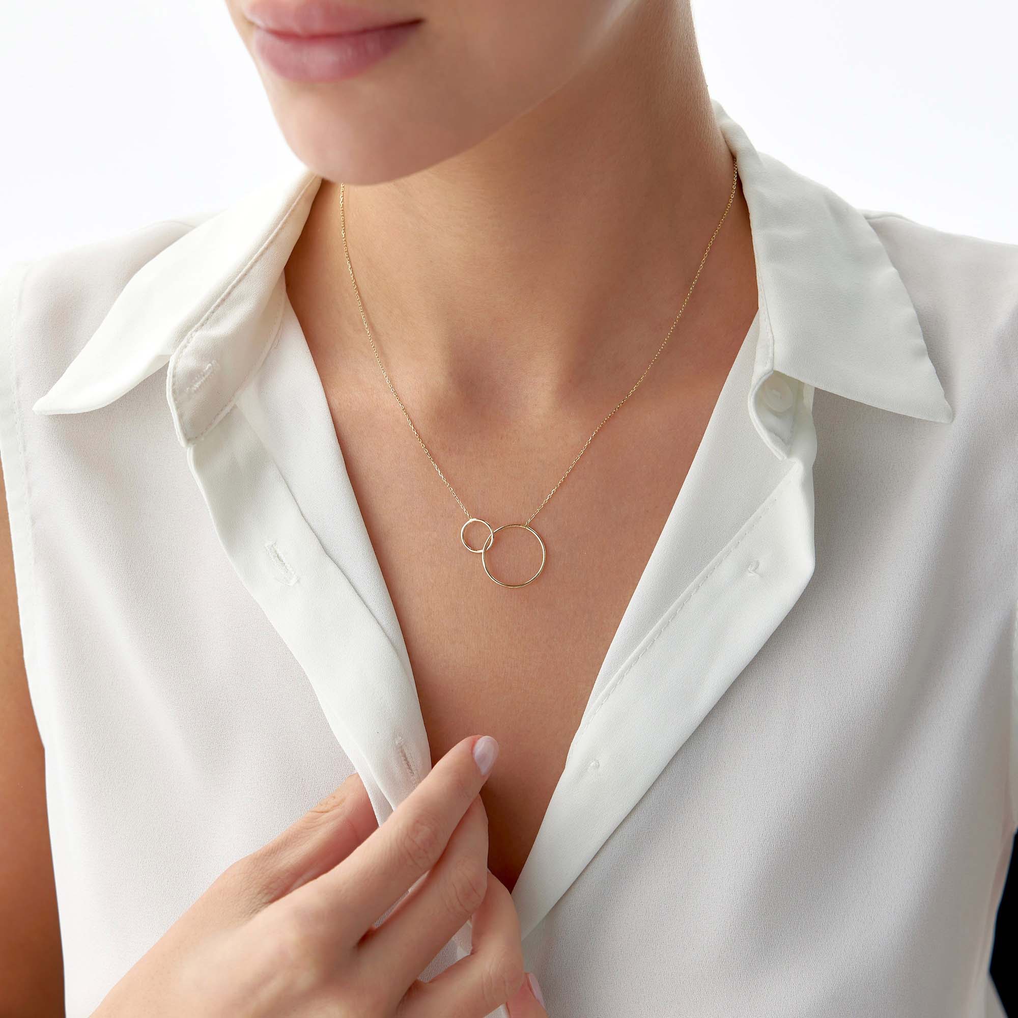 Gold necklace with a double-circle pendant worn by a person in a white shirt.