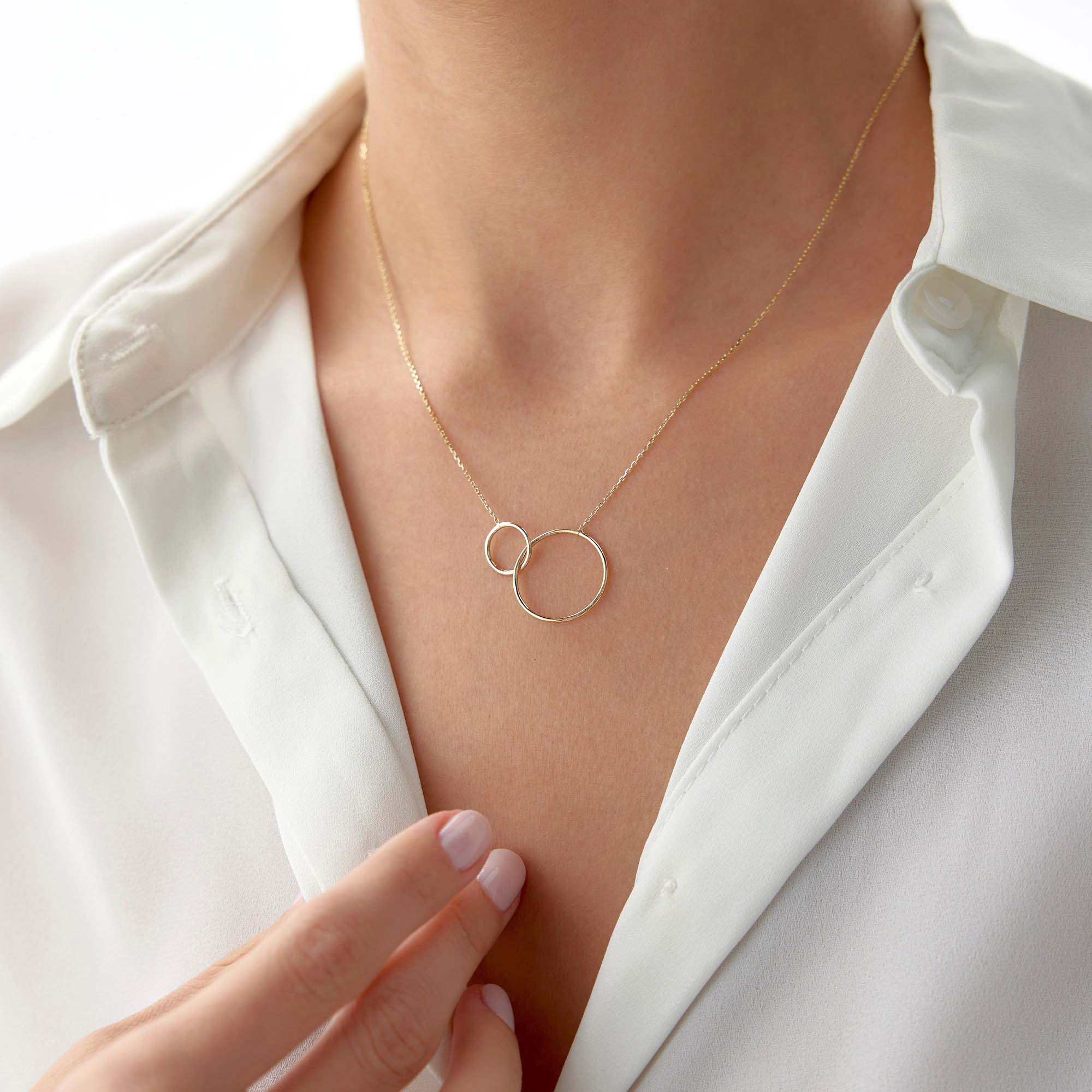 Gold necklace with a double-circle pendant worn by a person in a white shirt.