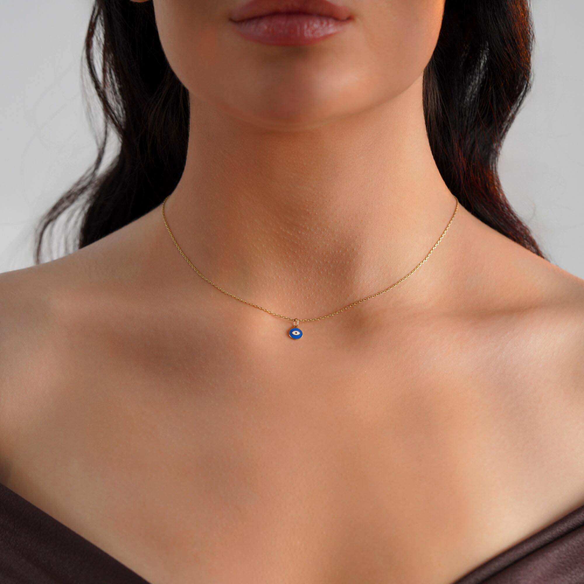A tiny eye pendant worn by a model on a thin gold chain.