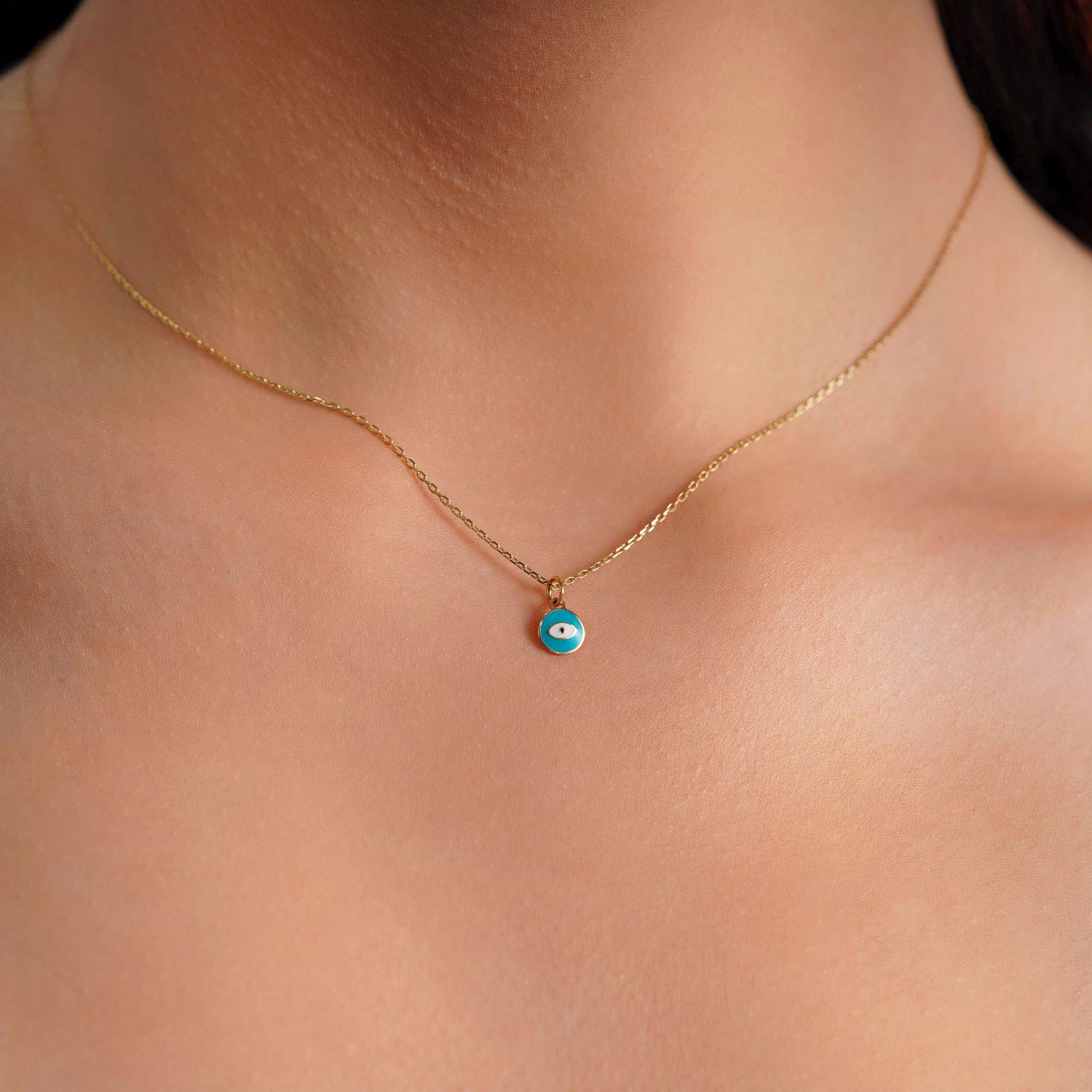 A model wearing a sky blue eye pendant on a thin gold chain.