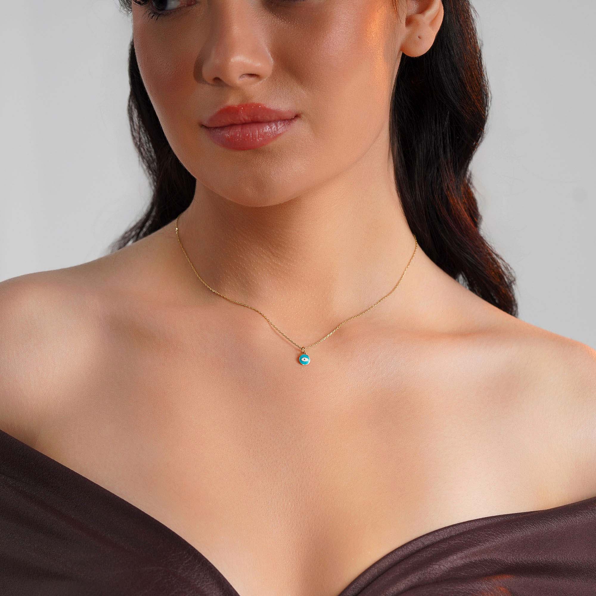 A model wearing a sky blue eye pendant on a thin gold chain.