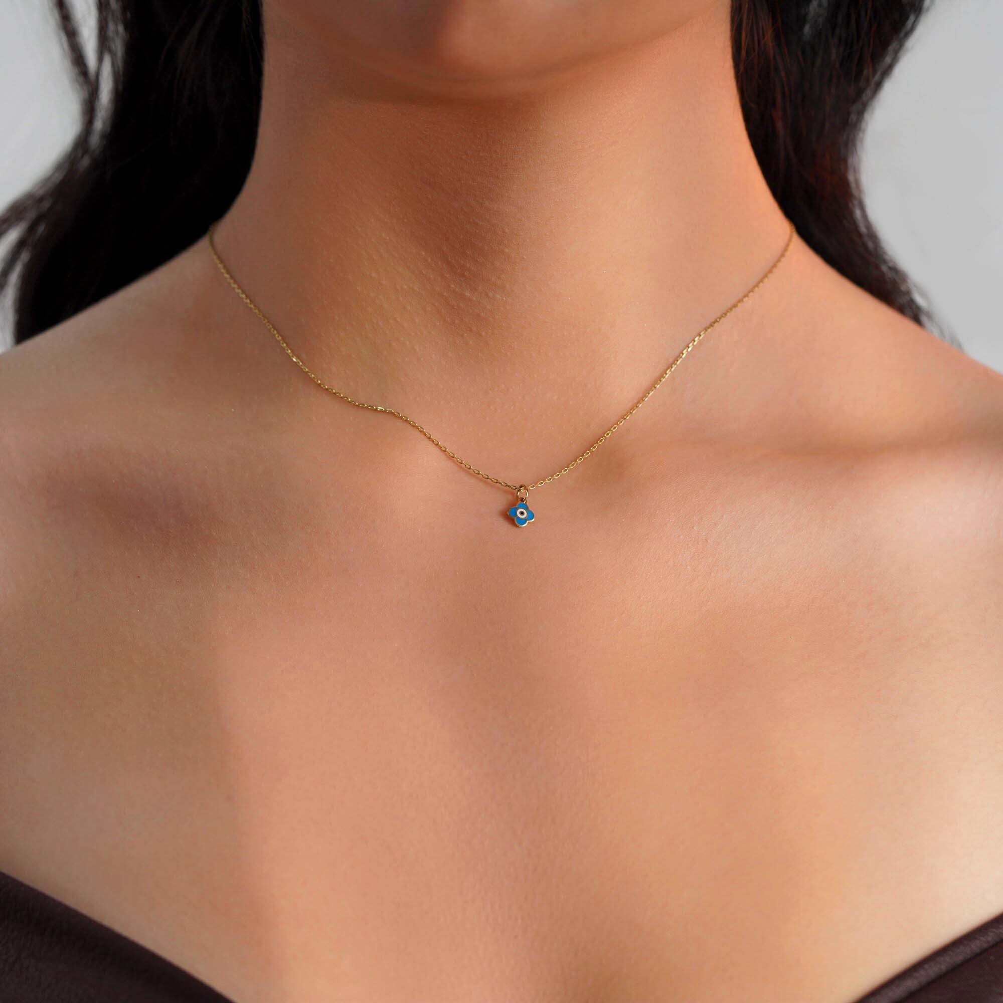 A model wearing a tiny clover pendant with an evil eye center worn on a thin gold chain.
