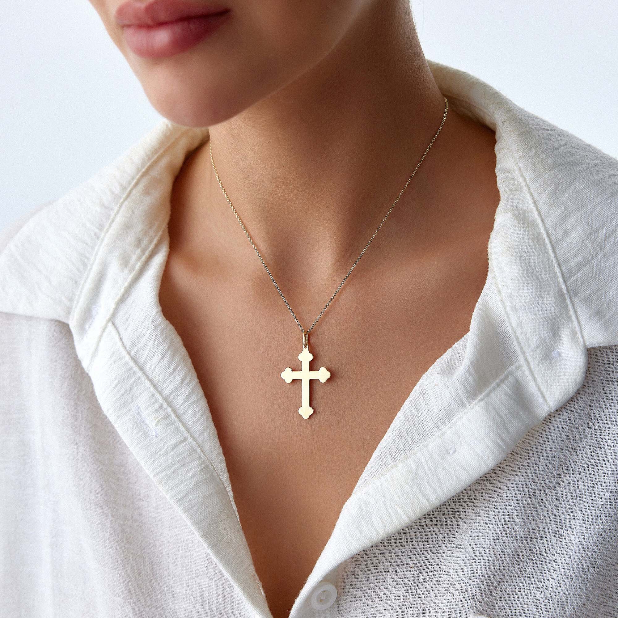 A large 14k yellow gold cross pendant necklace worn by a model with a white shirt