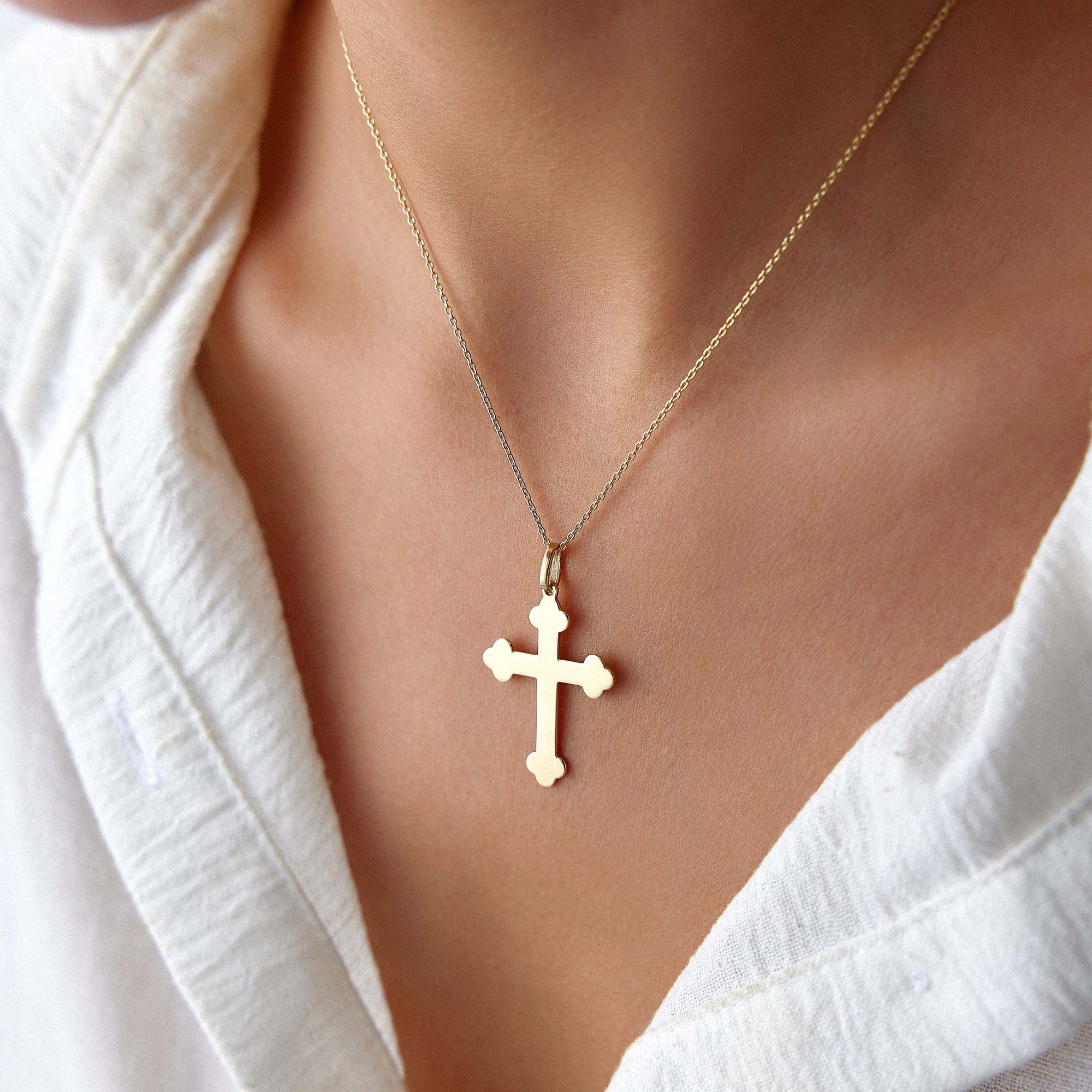 A large 14k yellow gold cross pendant necklace worn by a model with a white shirt