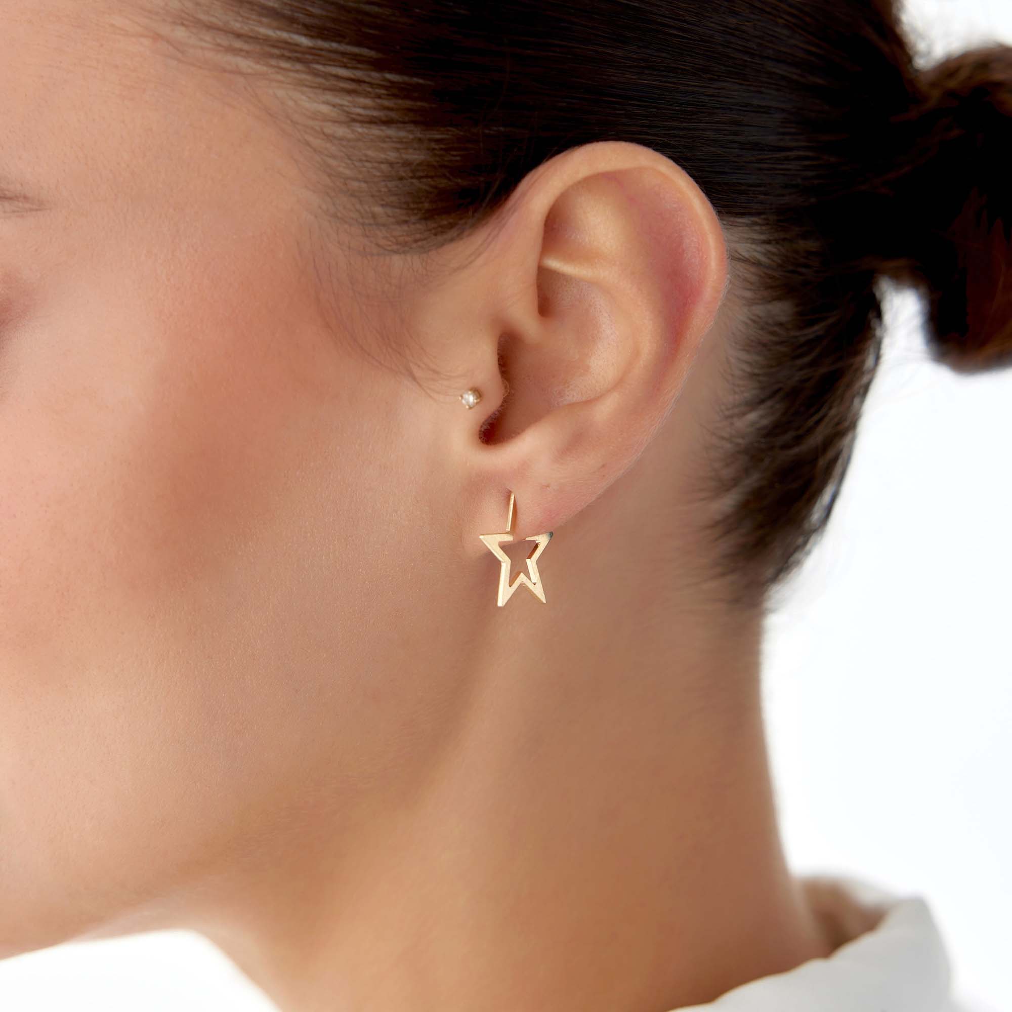Gold star-shaped earring worn by a person on a white background