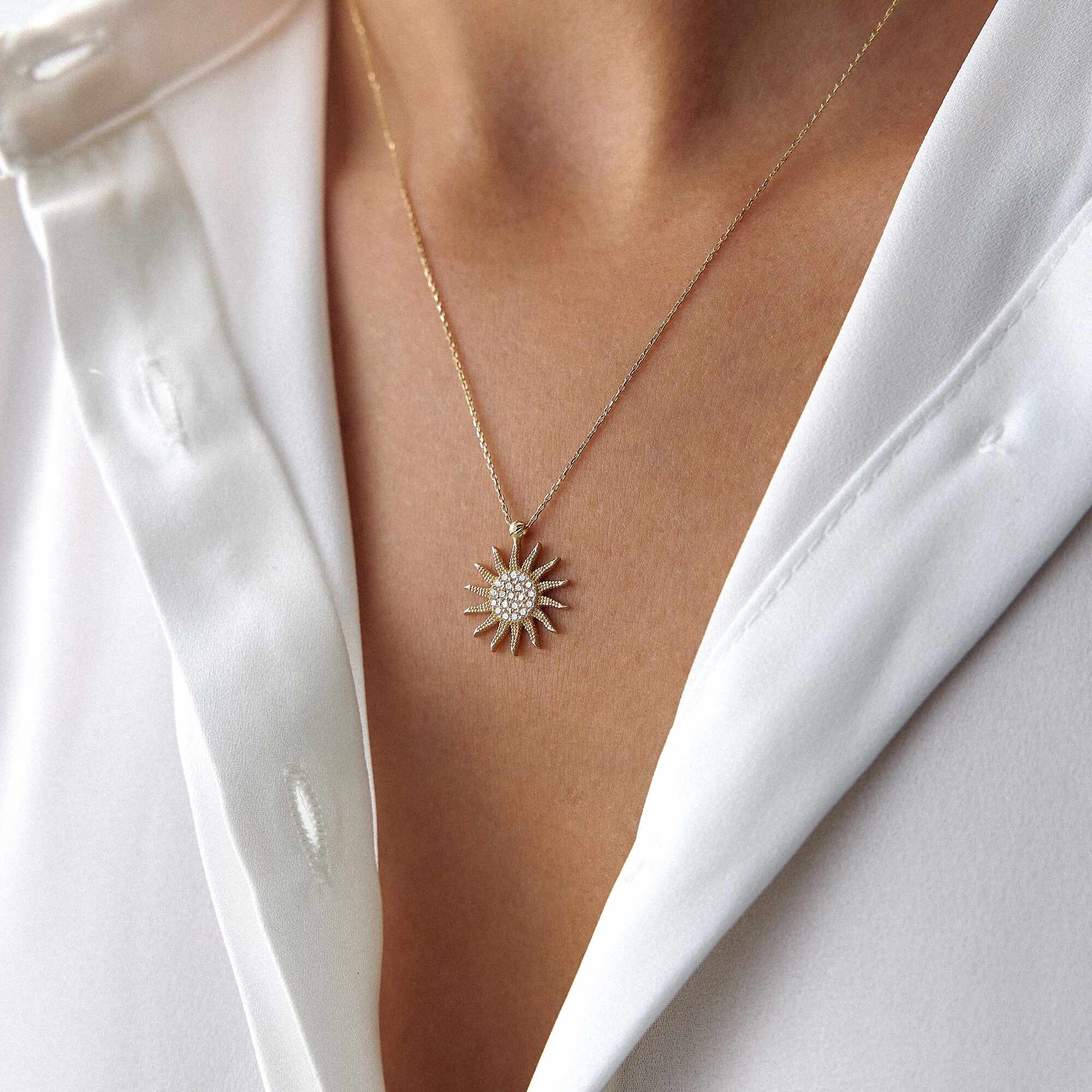 Person wearing a white sleeveless top with a necklace featuring a sun design.