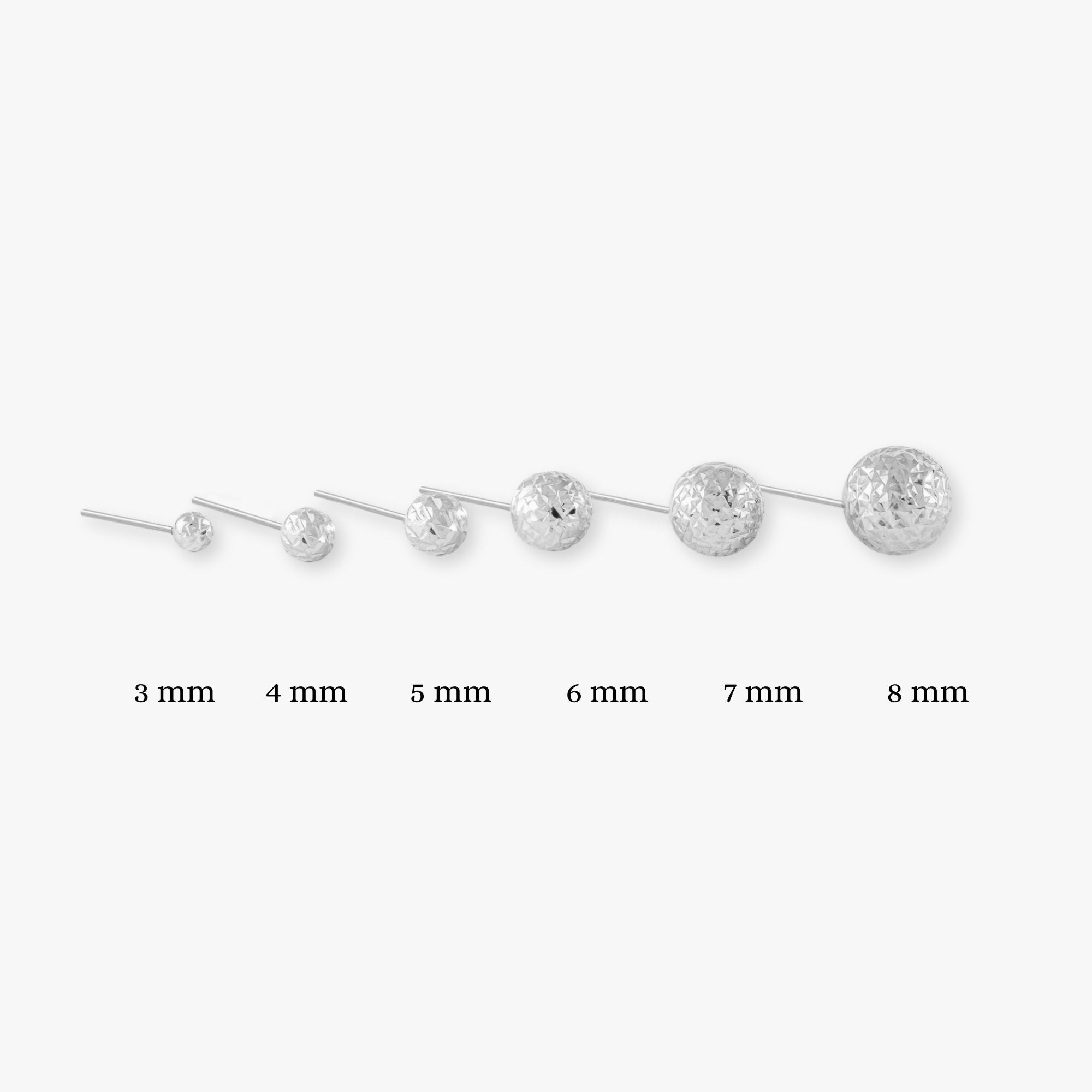 A selection of single 14k white gold laser cut sphere studs in various sizes, displayed in a row with their corresponding sizes labeled, on a white background.