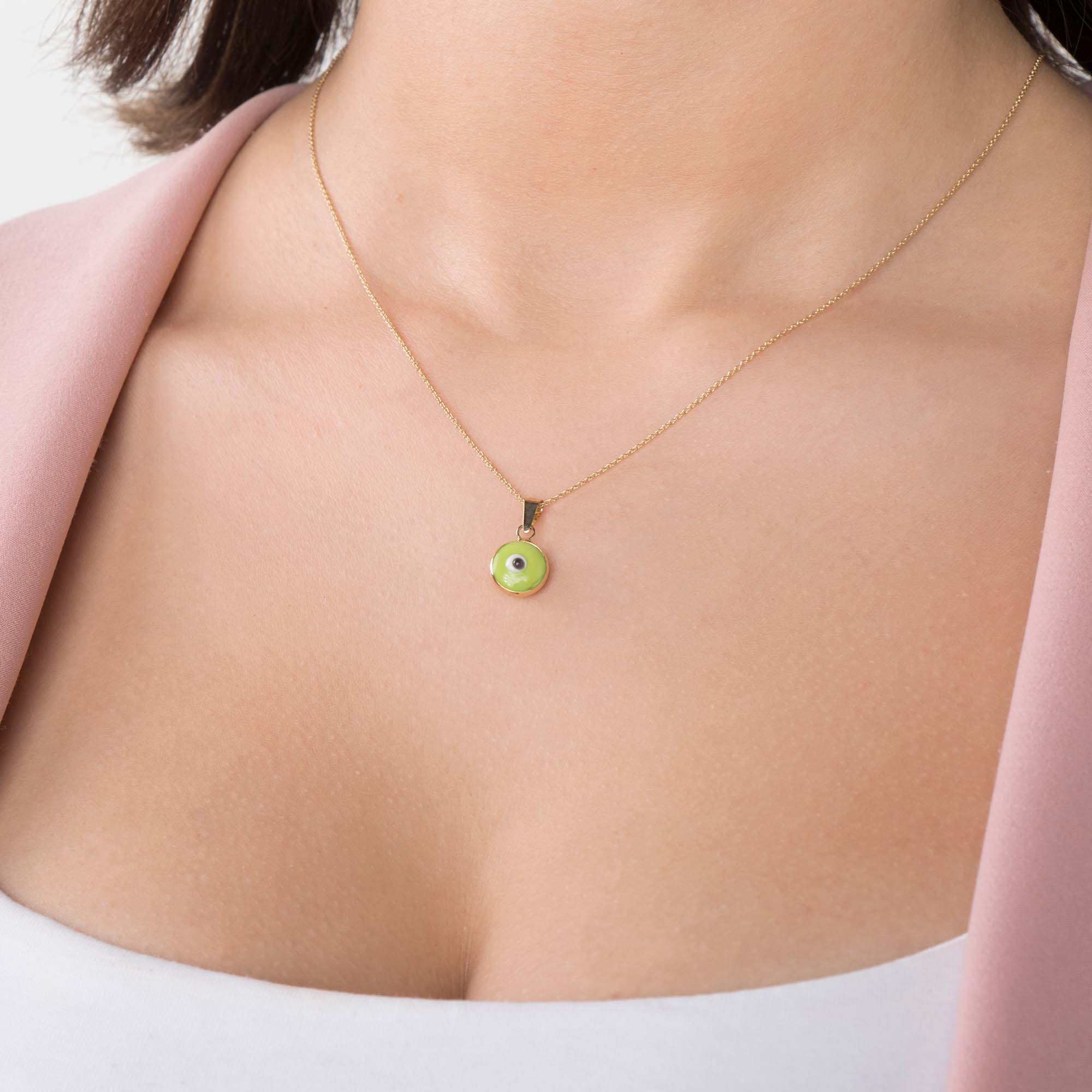 A model wearing a lime green evil eye pendant on a thin gold chain
