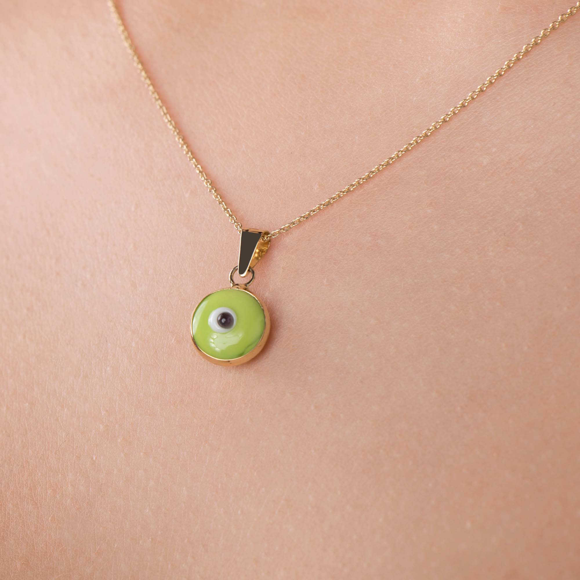 A lime green evil eye pendant on a thin gold chain shown up-close