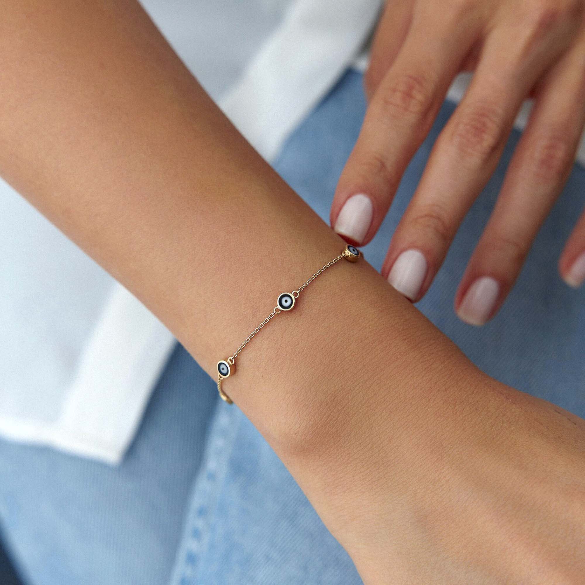 14k yellow gold black evil eye bracelet with 7 evil eyes shown on a wrist