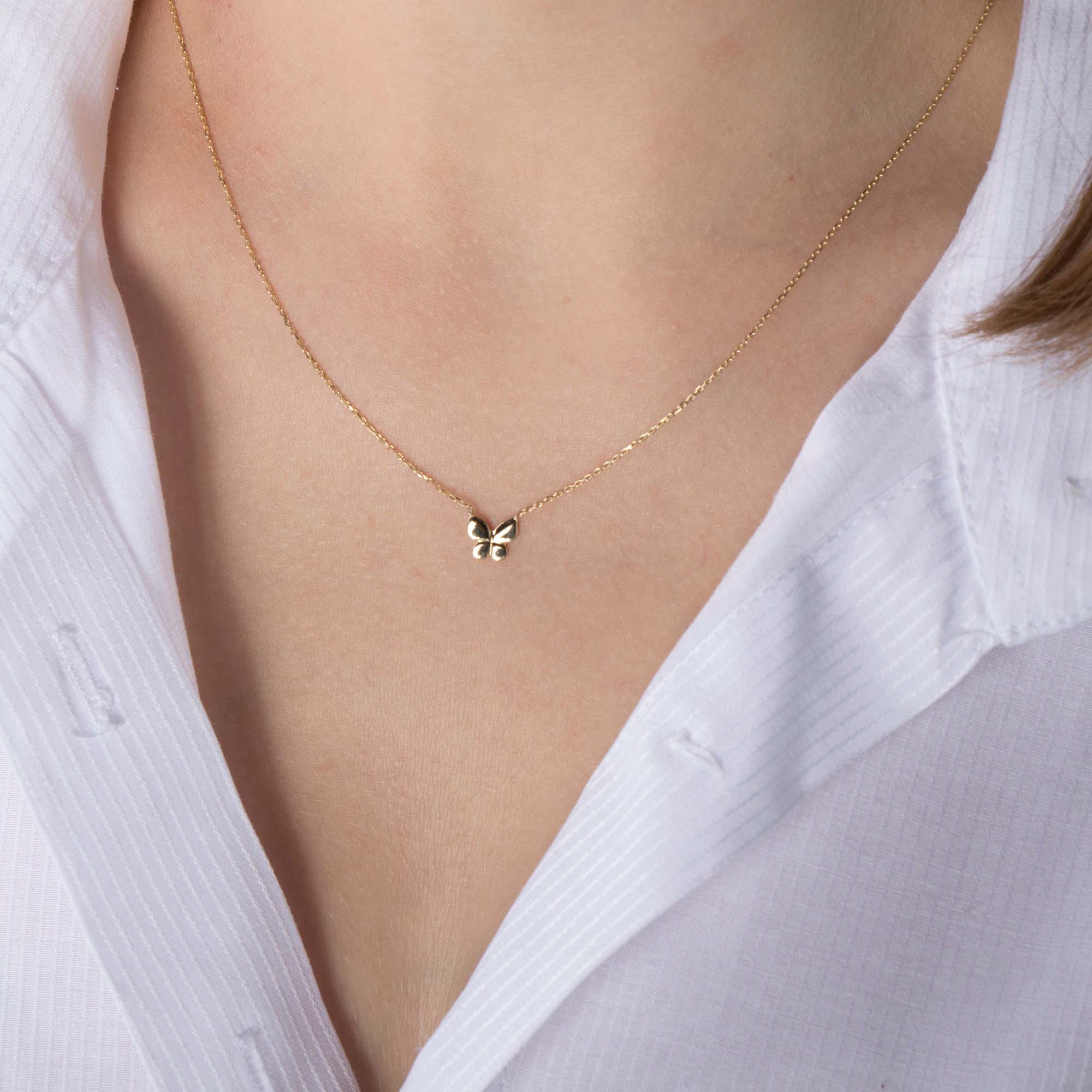 A minimal gold butterfly necklace on a person's neck with a white shirt background