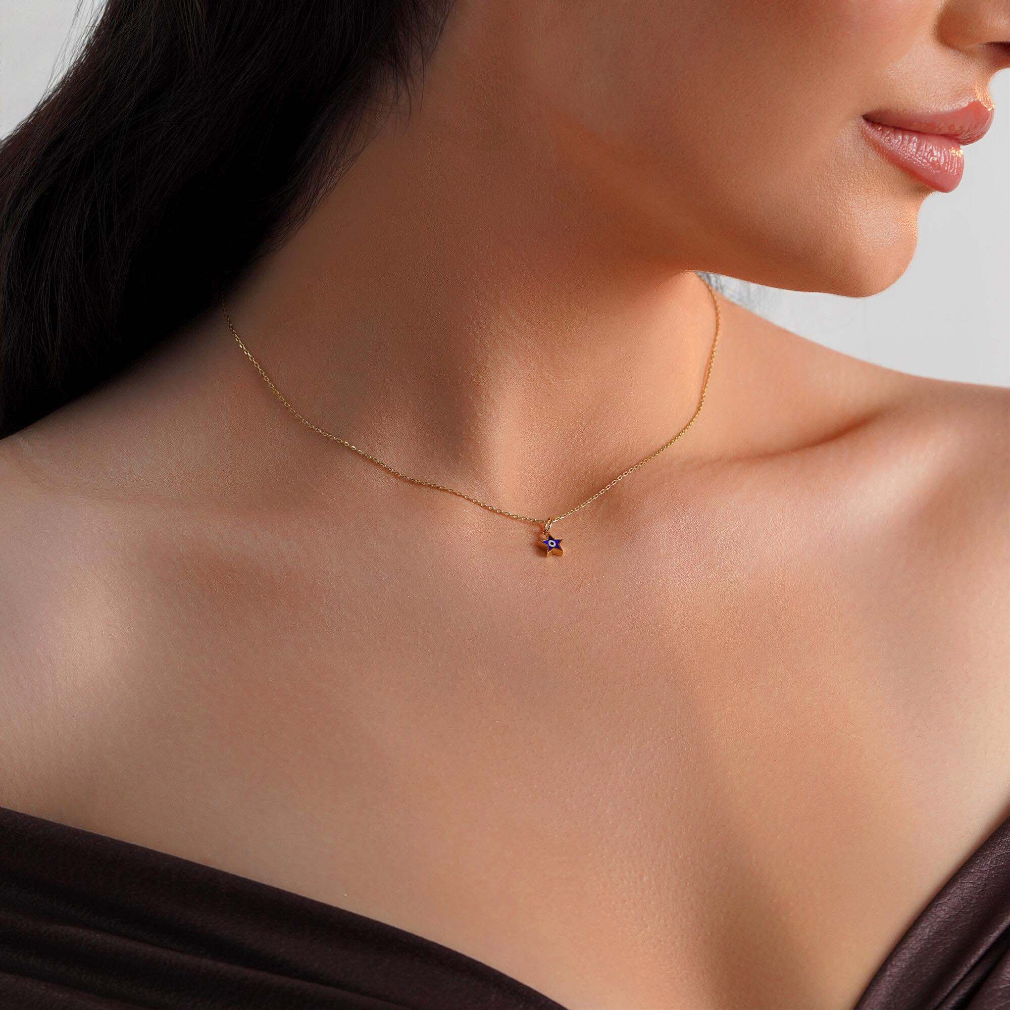 A model wearing a tiny star pendant with an evil eye center on a thin gold chain