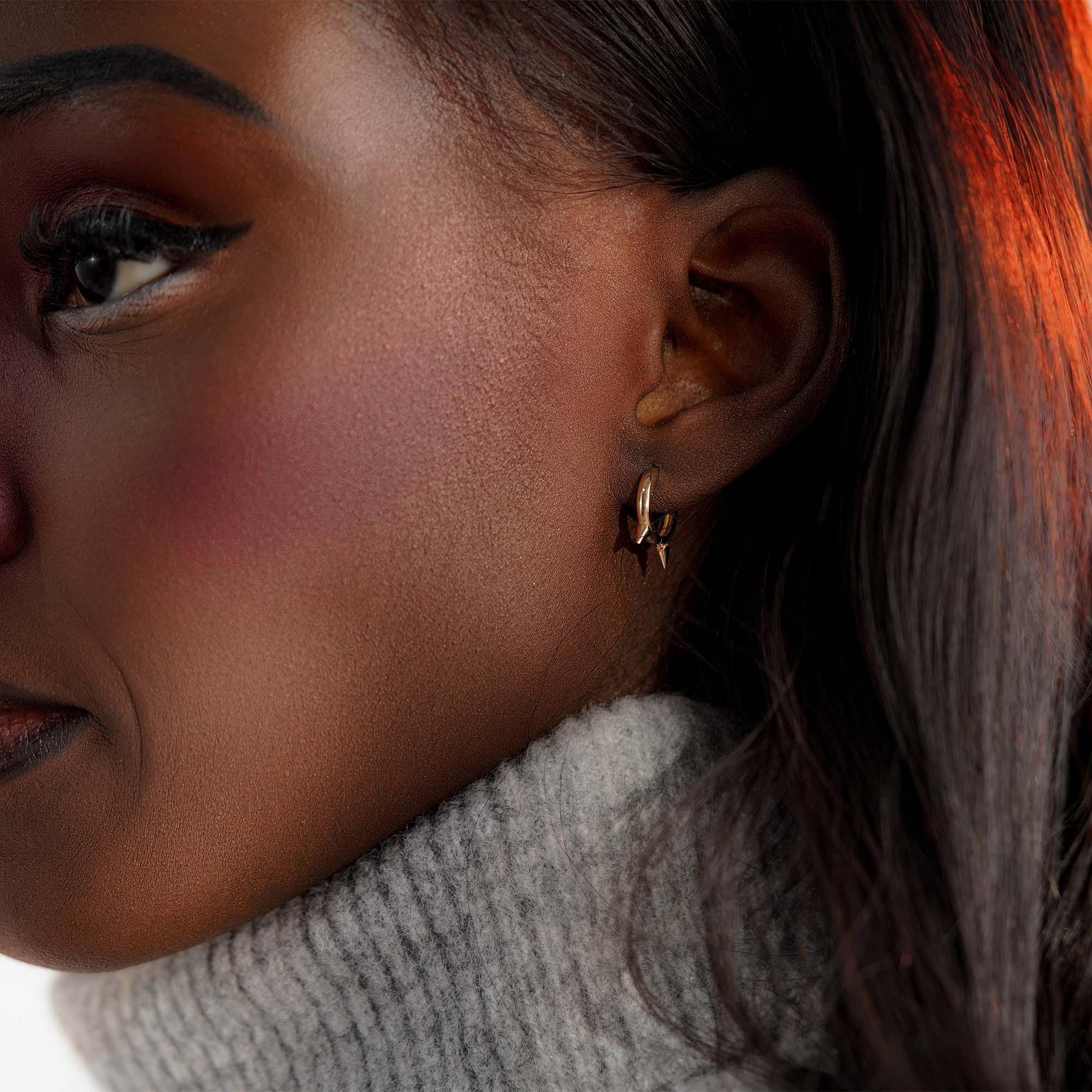 Close-up of a person wearing a gold hoop with golden spikes.