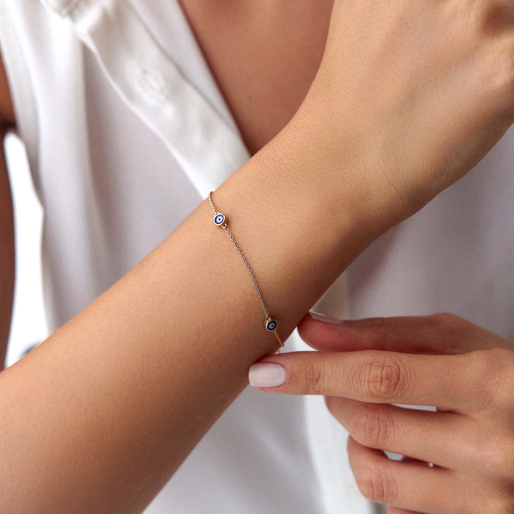 A 14 karat yellow gold bracelet with three navy blue evil eye charms on a wrist